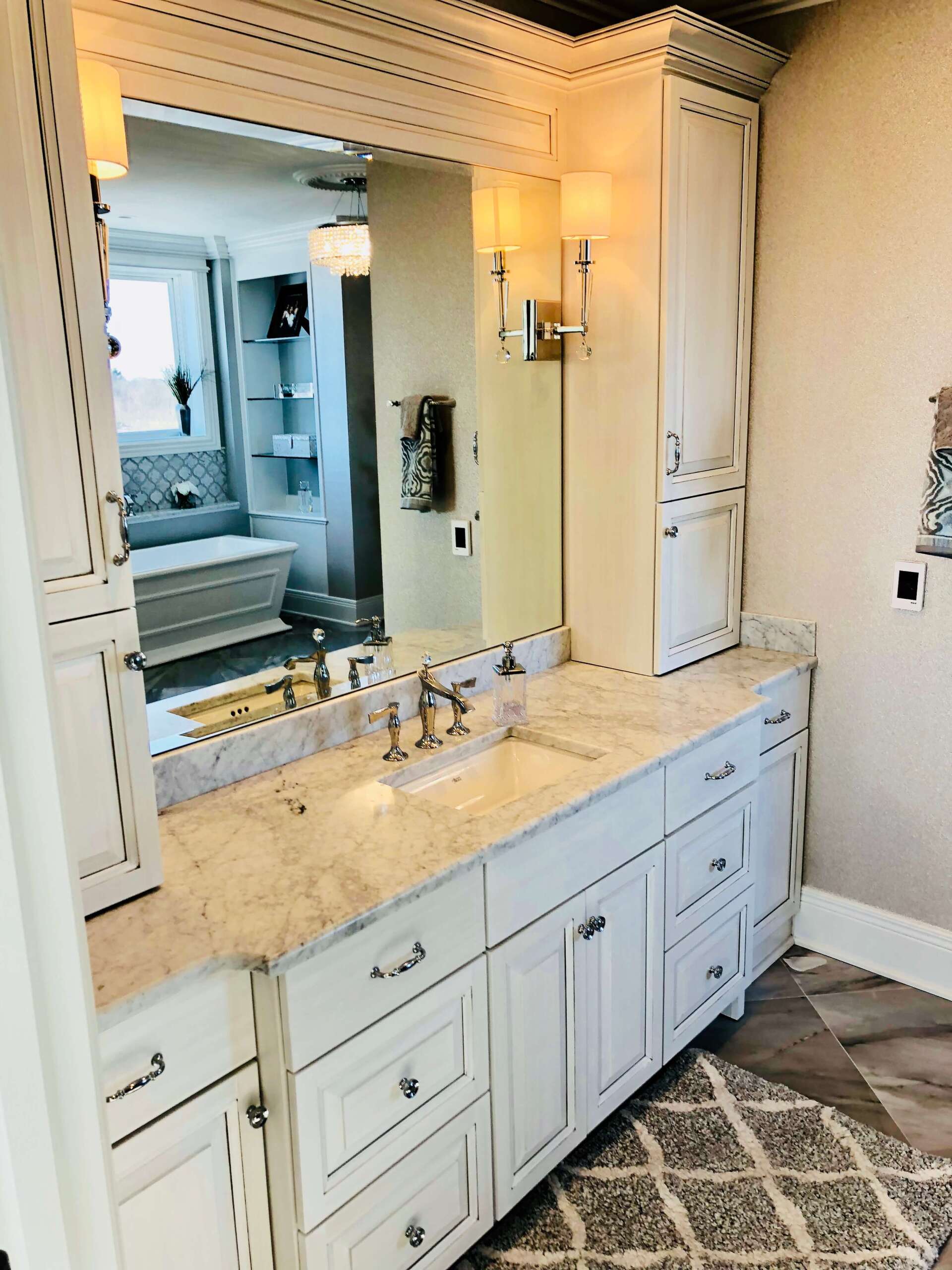 Elegant bathroom vanity with marble countertop, mirror, brass sconces, and white cabinets