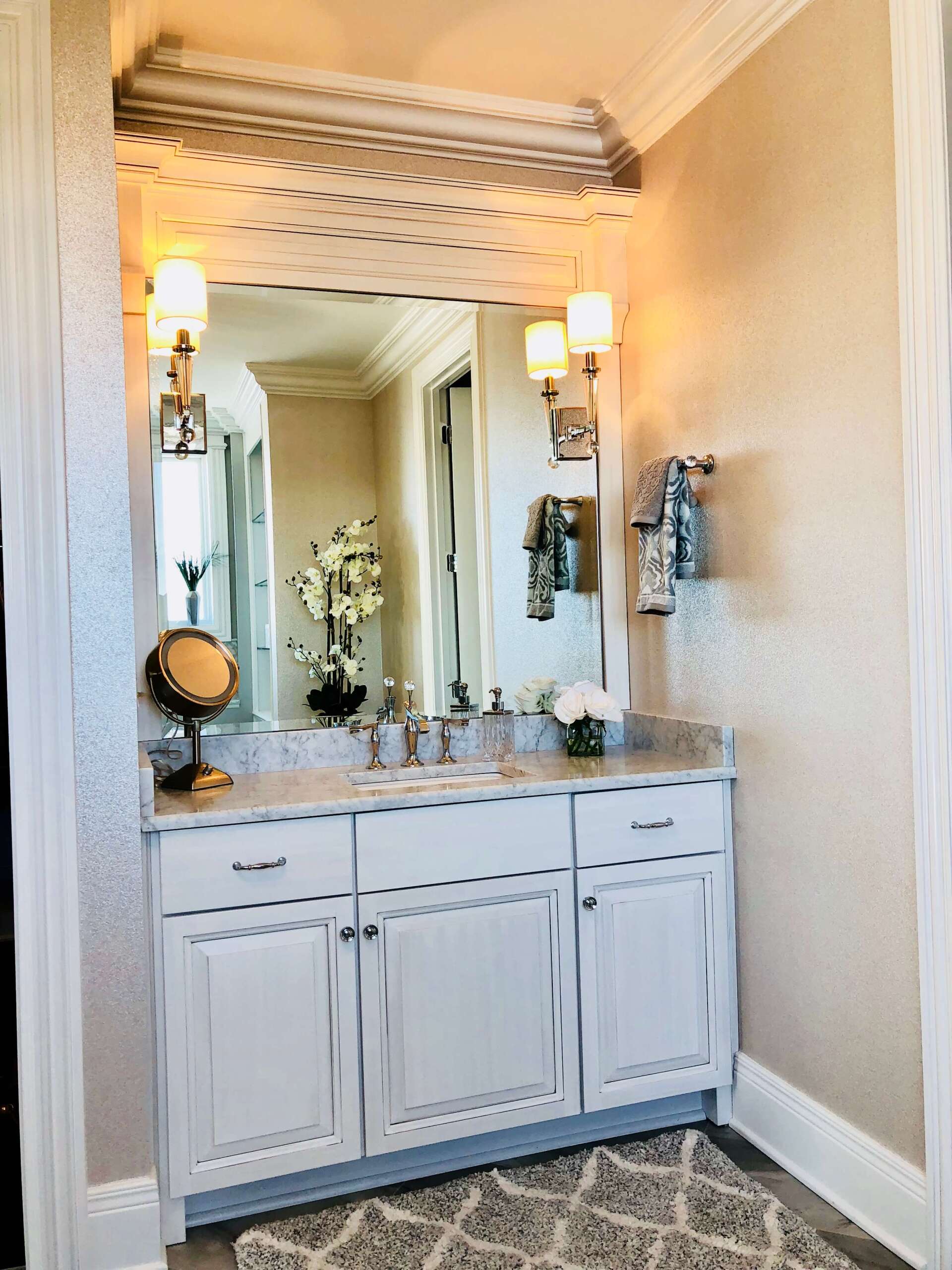 White bathroom vanity with mirror, wall sconces, and marble countertop in a narrow hallway setting