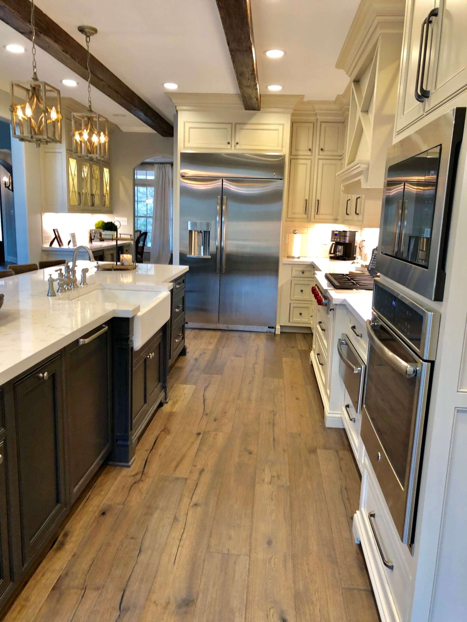 Bright, narrow kitchen with white countertops, dark cabinets, stainless steel fridge, and hardwood floors