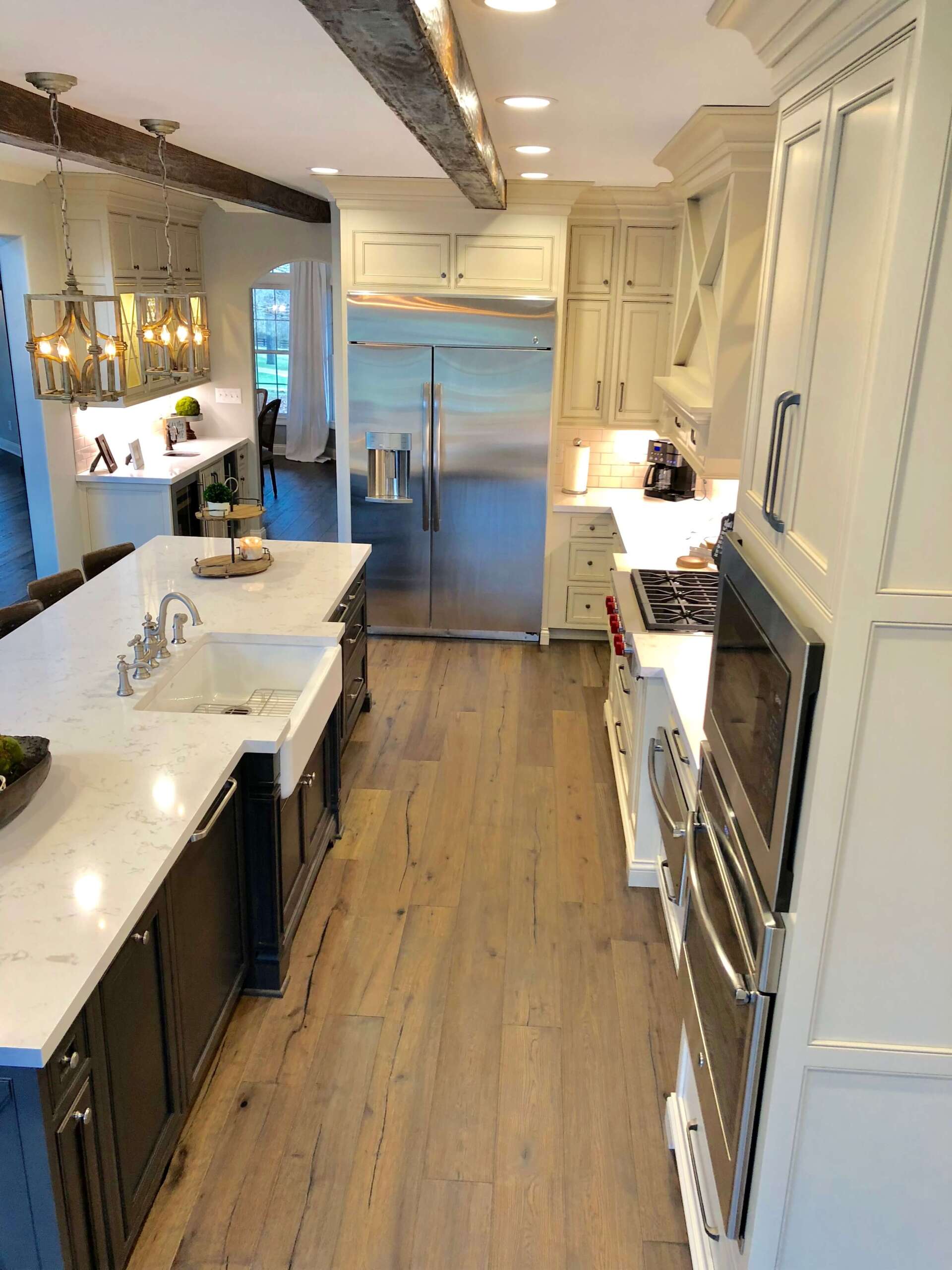 Bright modern kitchen with white cabinets, marble counters, wood floor, and ocean view through glass doors