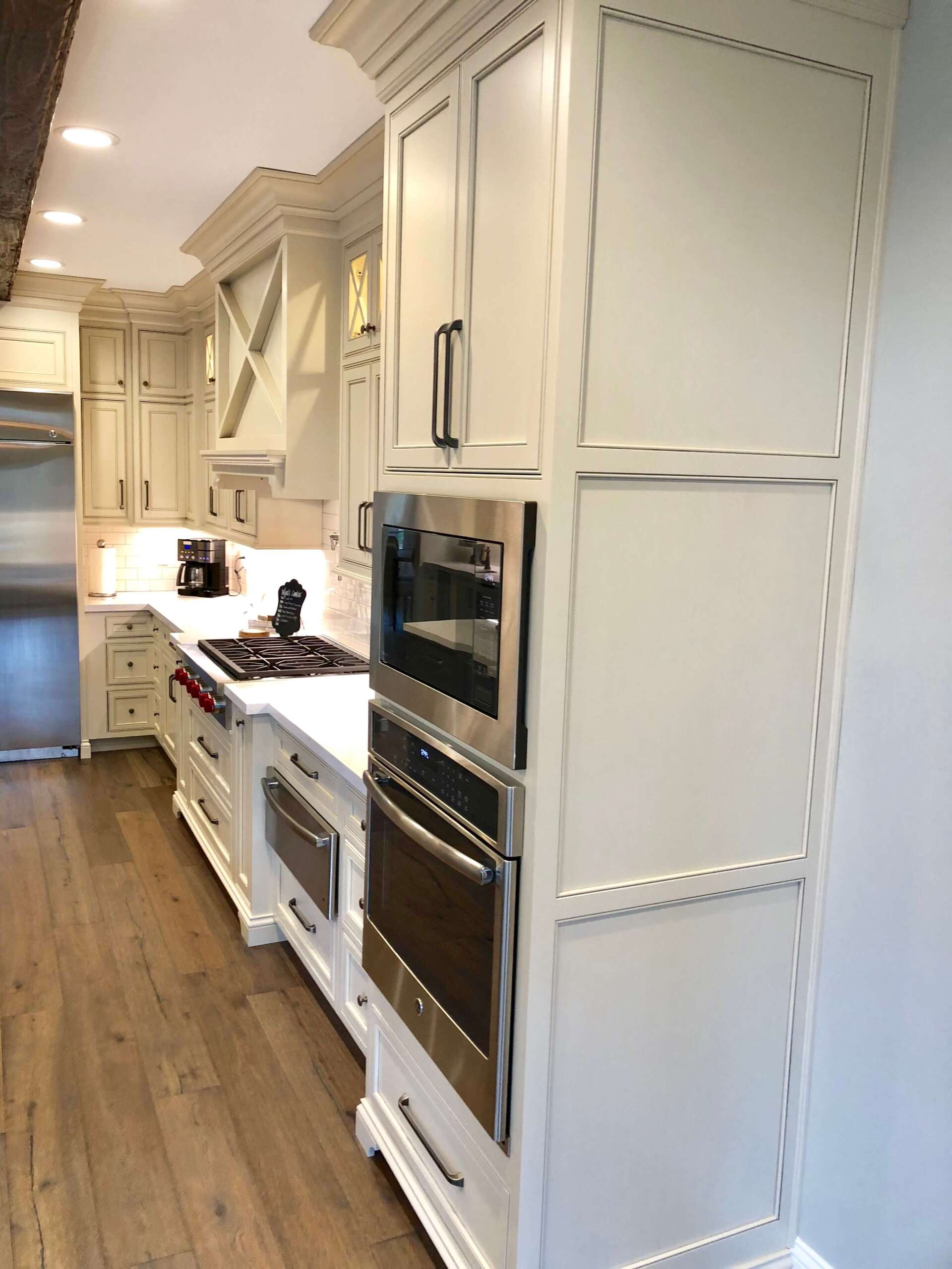 Bright white galley kitchen with built-in ovens, cabinets, and wood flooring