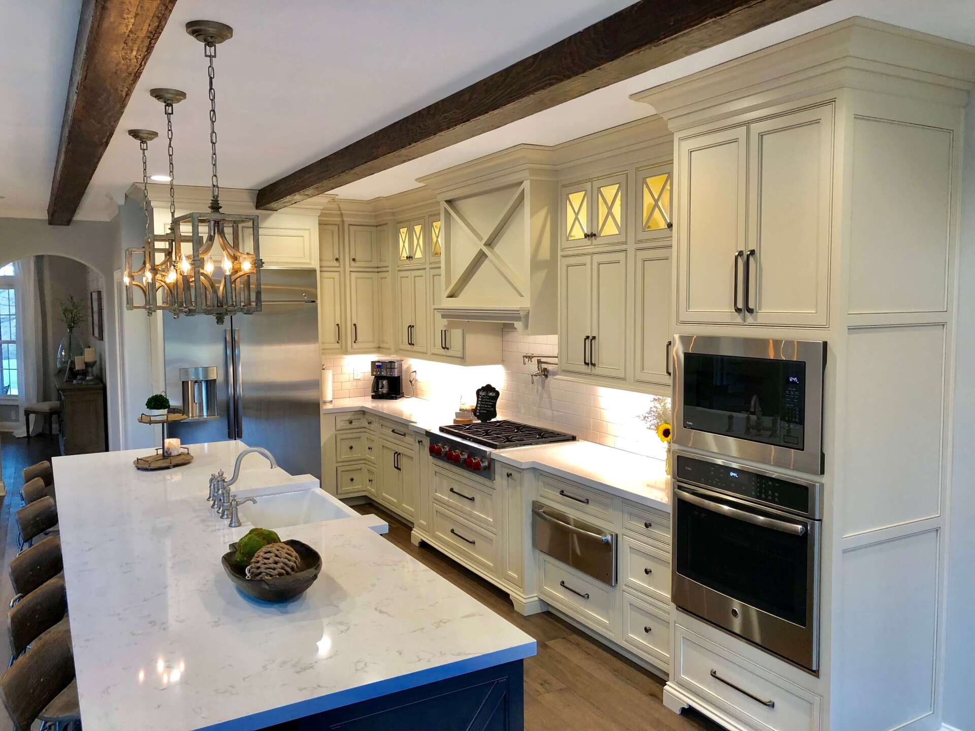 Modern white kitchen with island, marble countertops, pendant lights, and built-in oven and cabinets