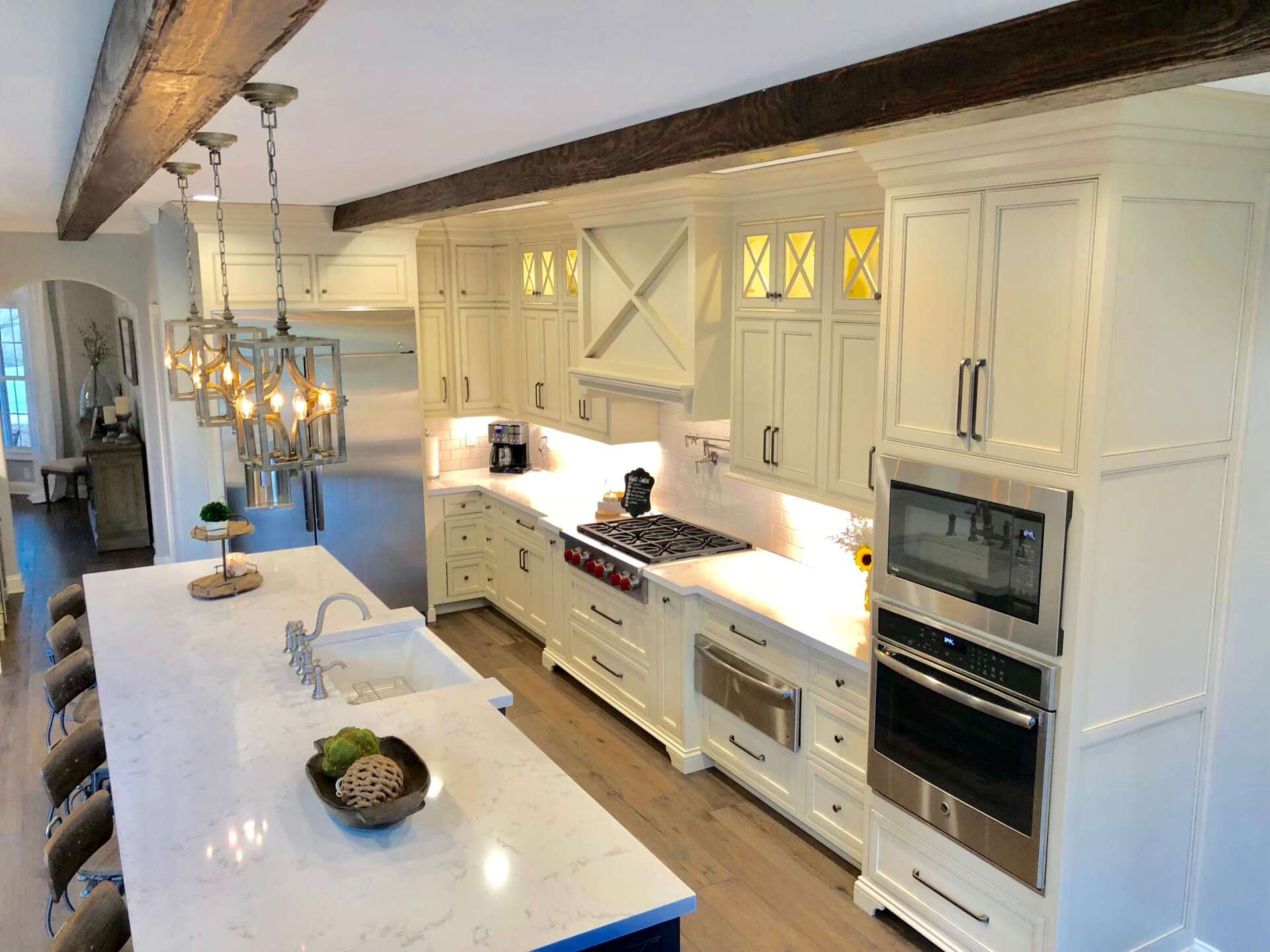 Bright white gourmet kitchen with island, farmhouse sink, chandelier, and built-in ovens