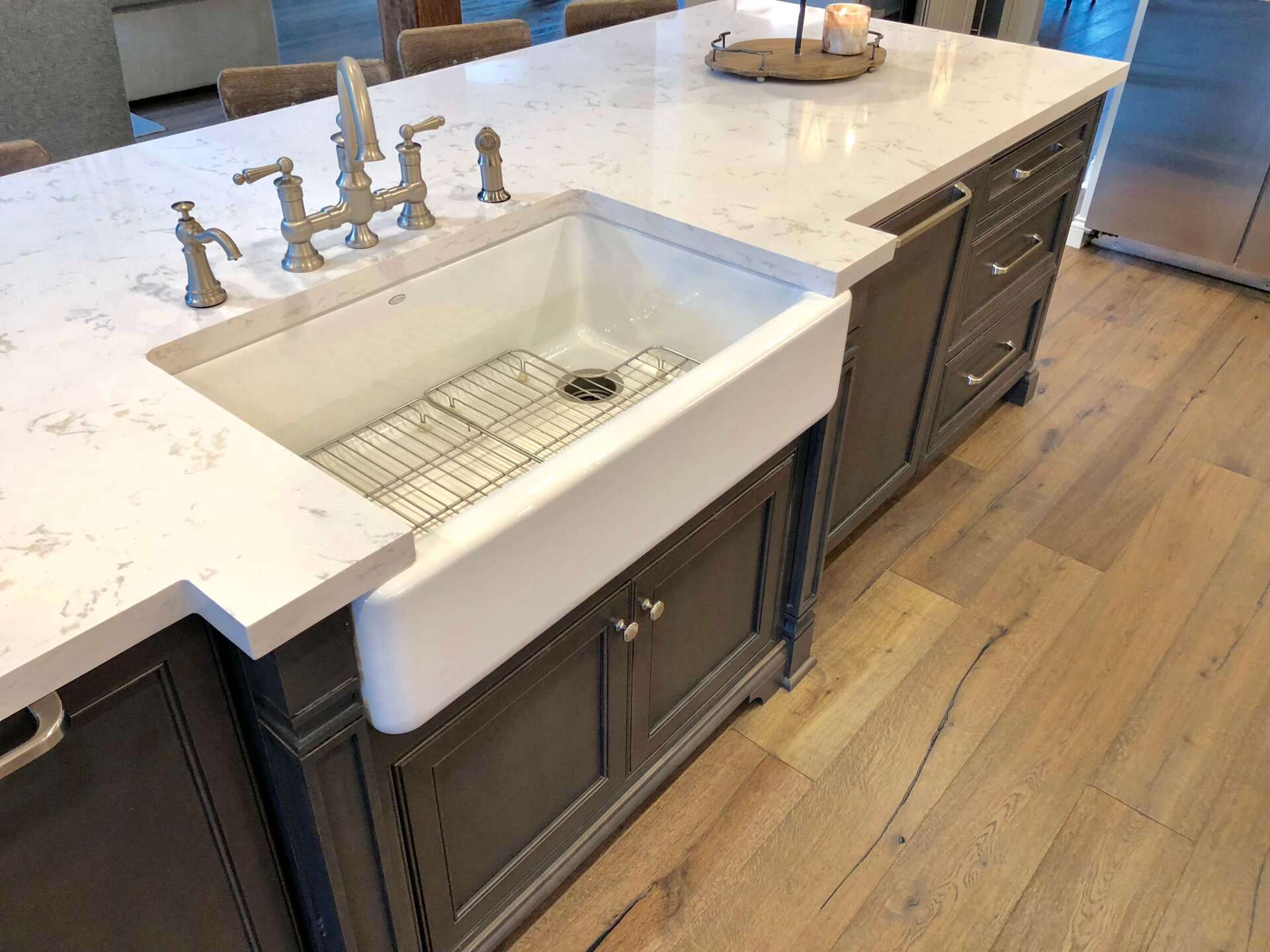 Kitchen island with farmhouse sink and silver faucet on a wood floor, next to a marble countertop