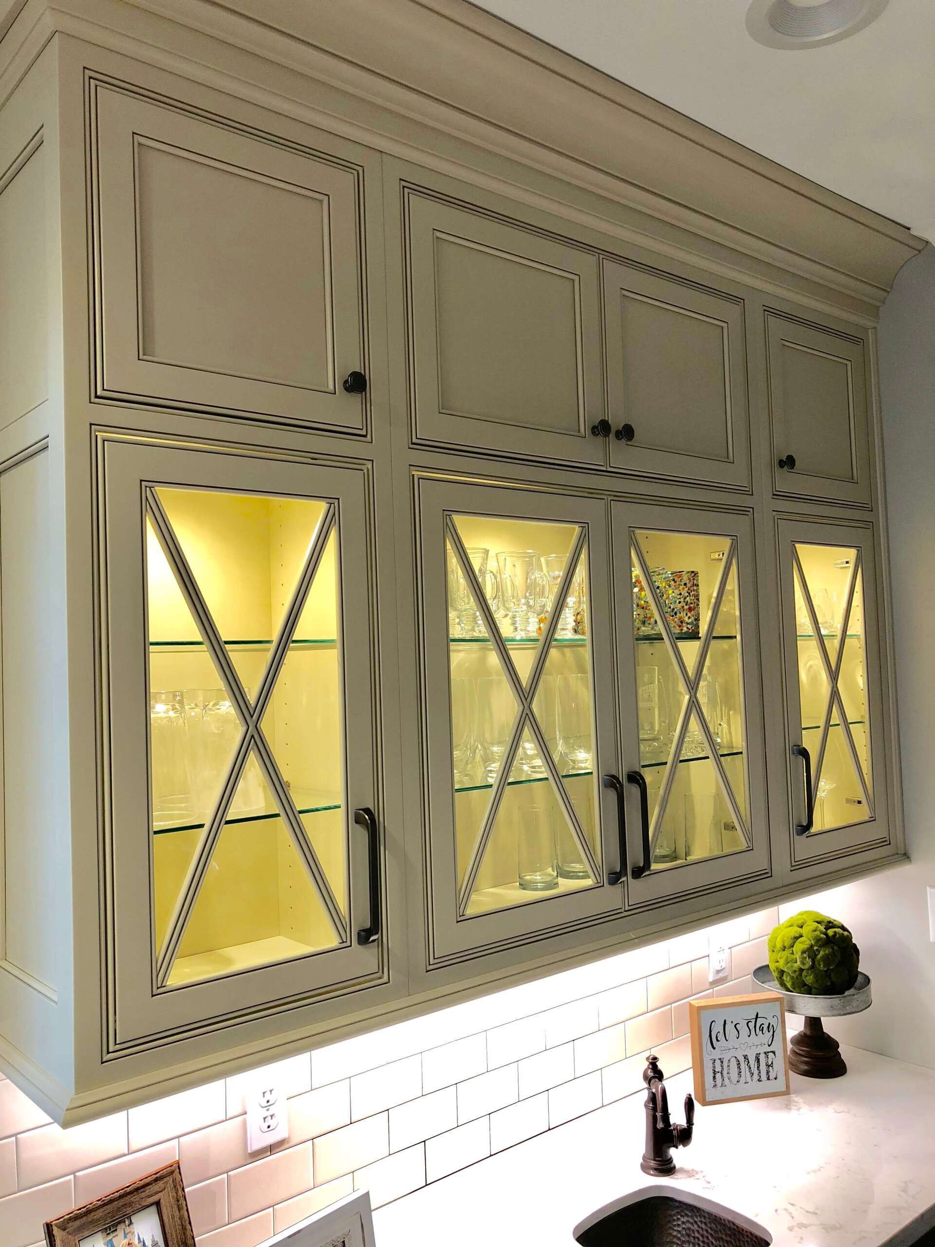 White kitchen cabinets with glass doors and warm under-cabinet lighting above a countertop.