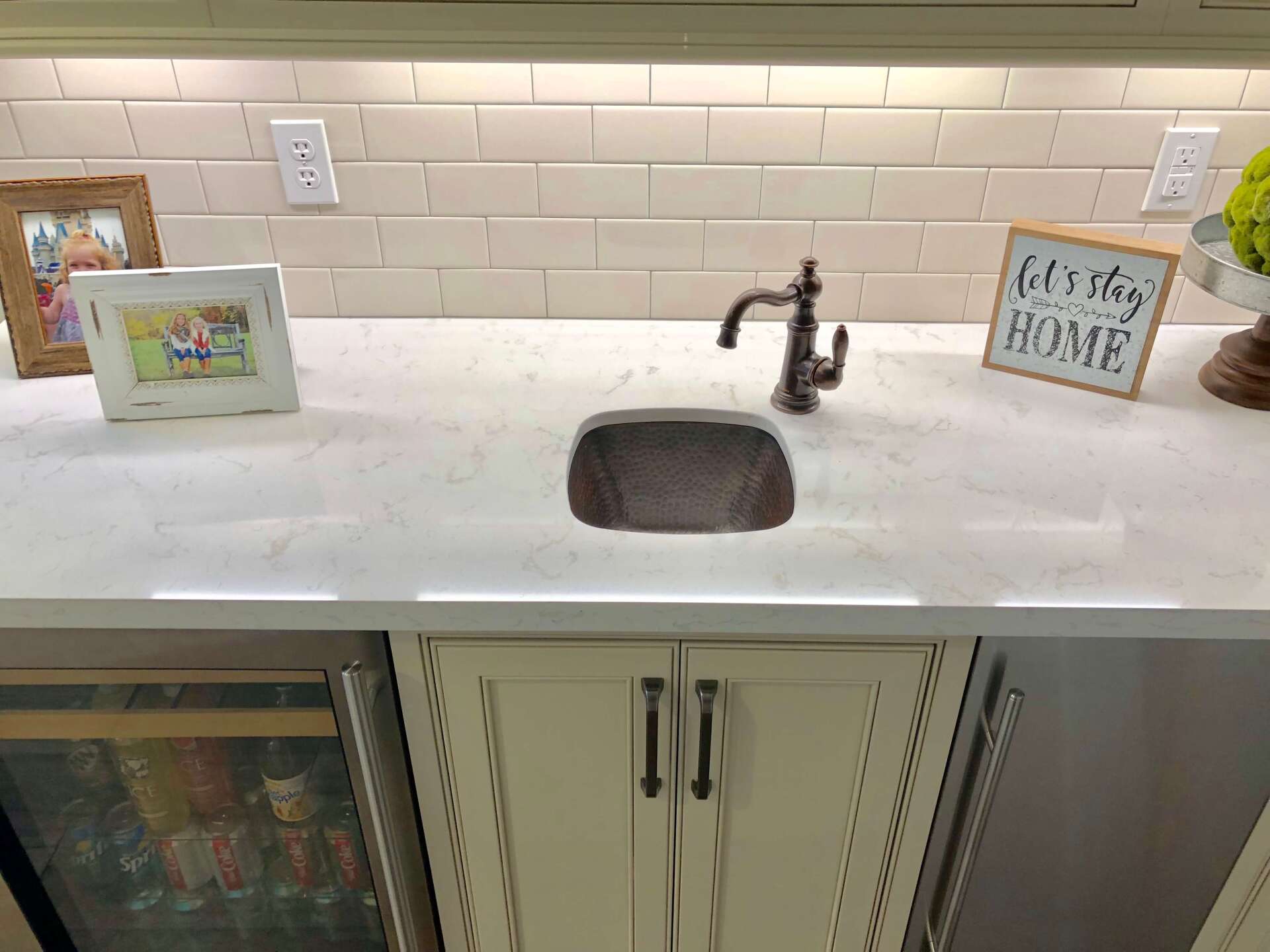 Kitchen sink with white countertop, dark faucet, framed photos, and subway tile backsplash