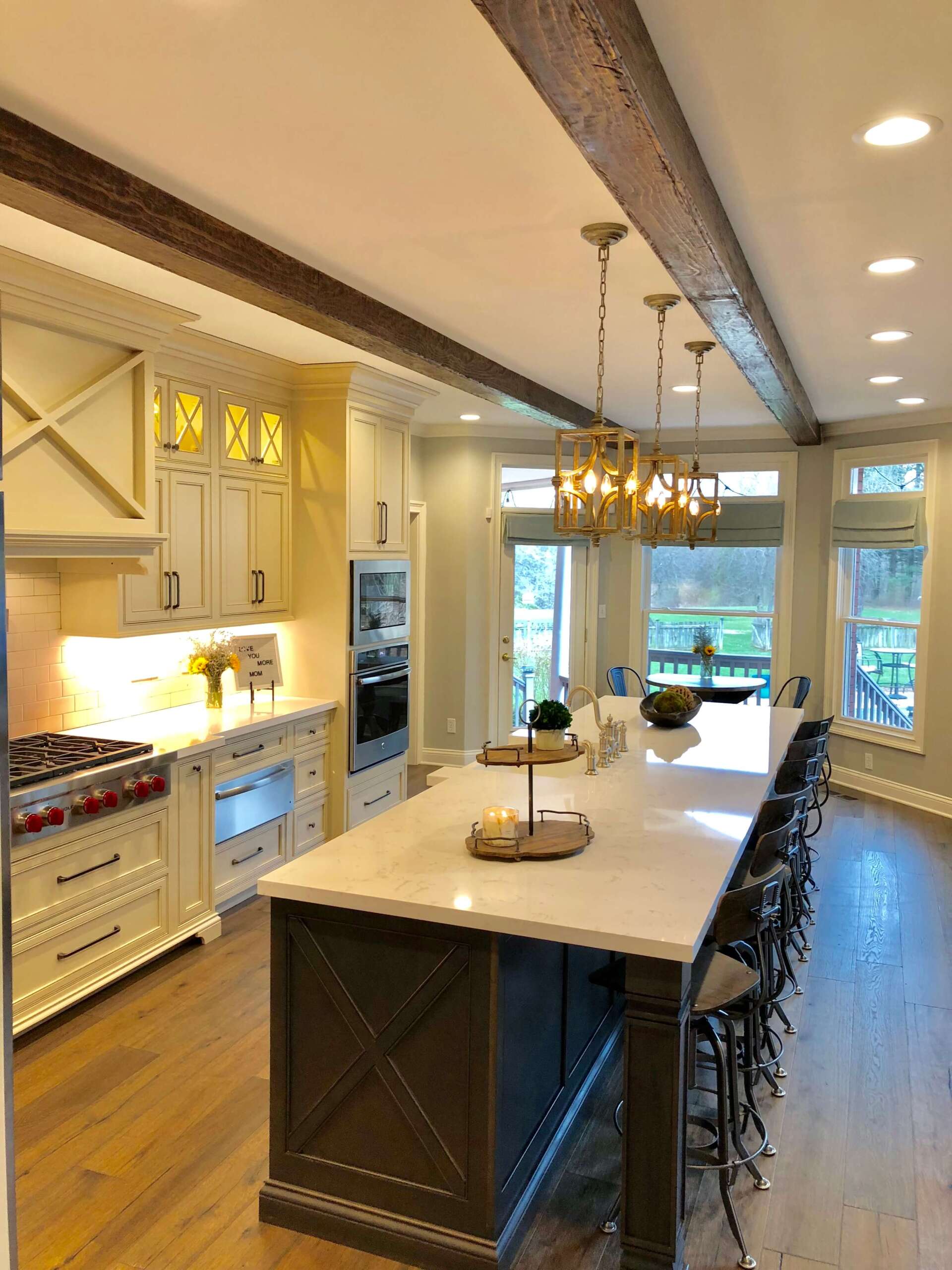 Bright modern kitchen with large island, white cabinets, and pendant lights overlooking a backyard.