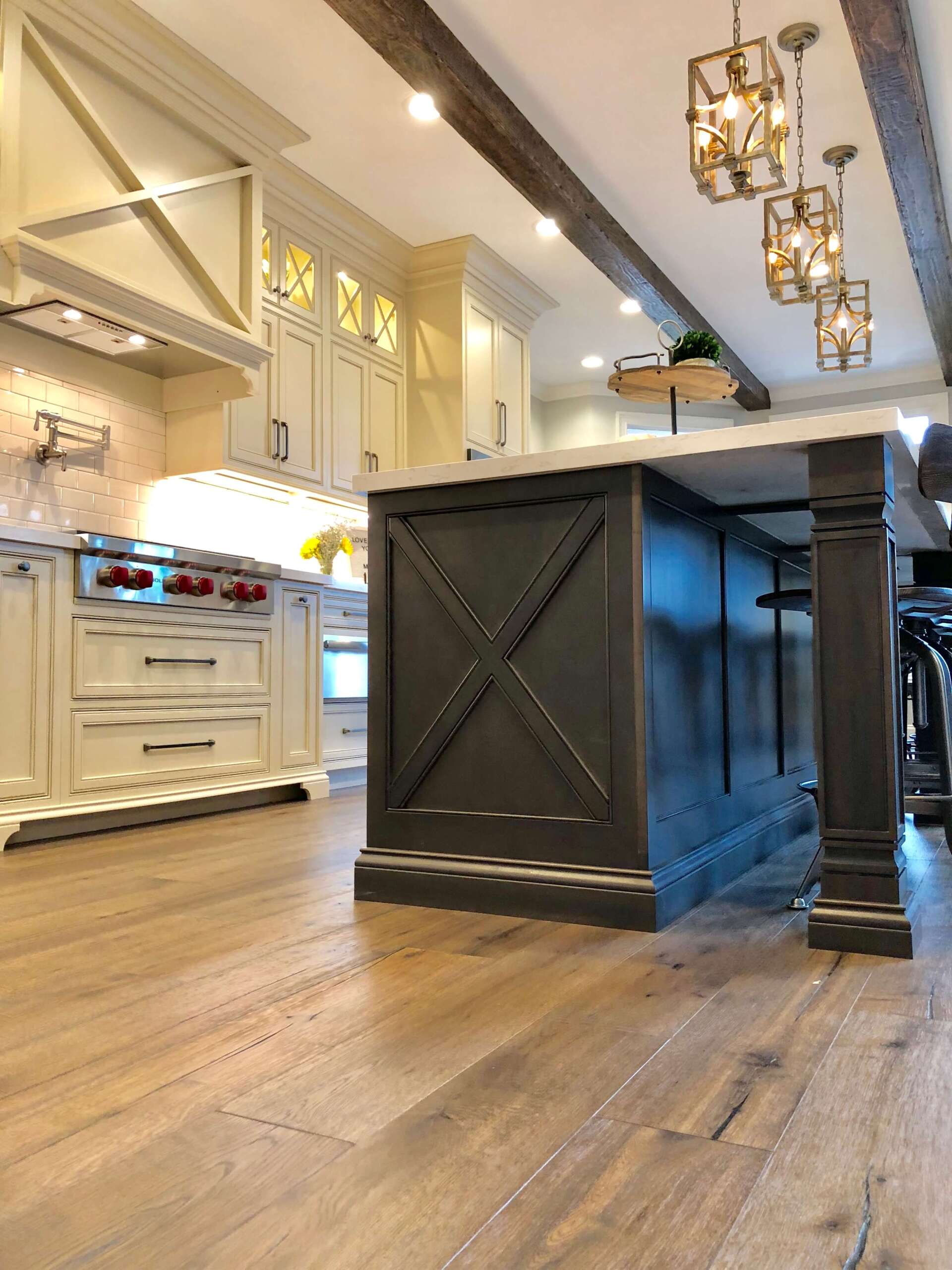 Bright kitchen with a large dark island, hardwood floors, white cabinets, and hanging pendant lights.