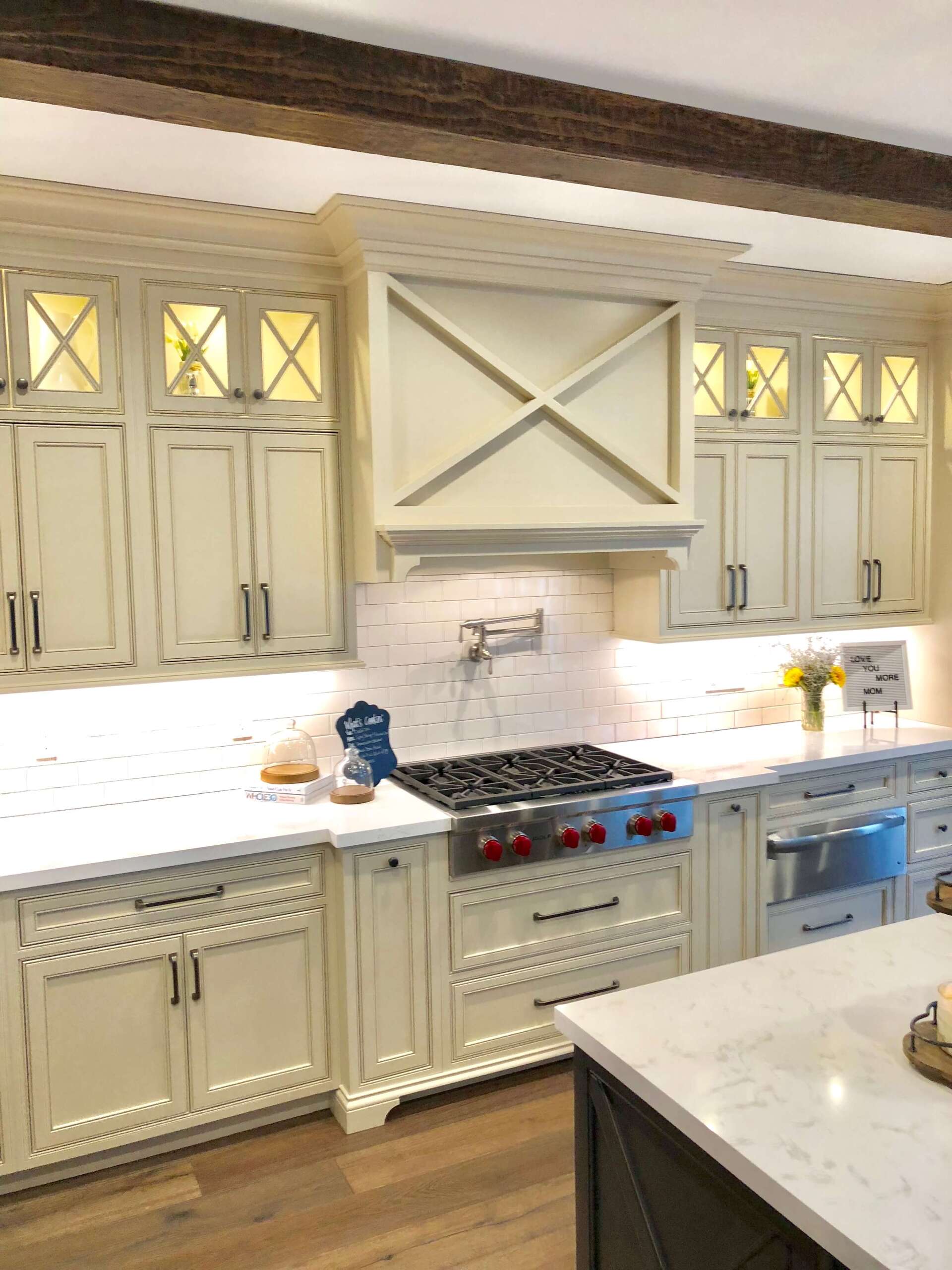 Elegant cream kitchen with tiled backsplash, gas range, glass-front cabinets, and marble island countertop