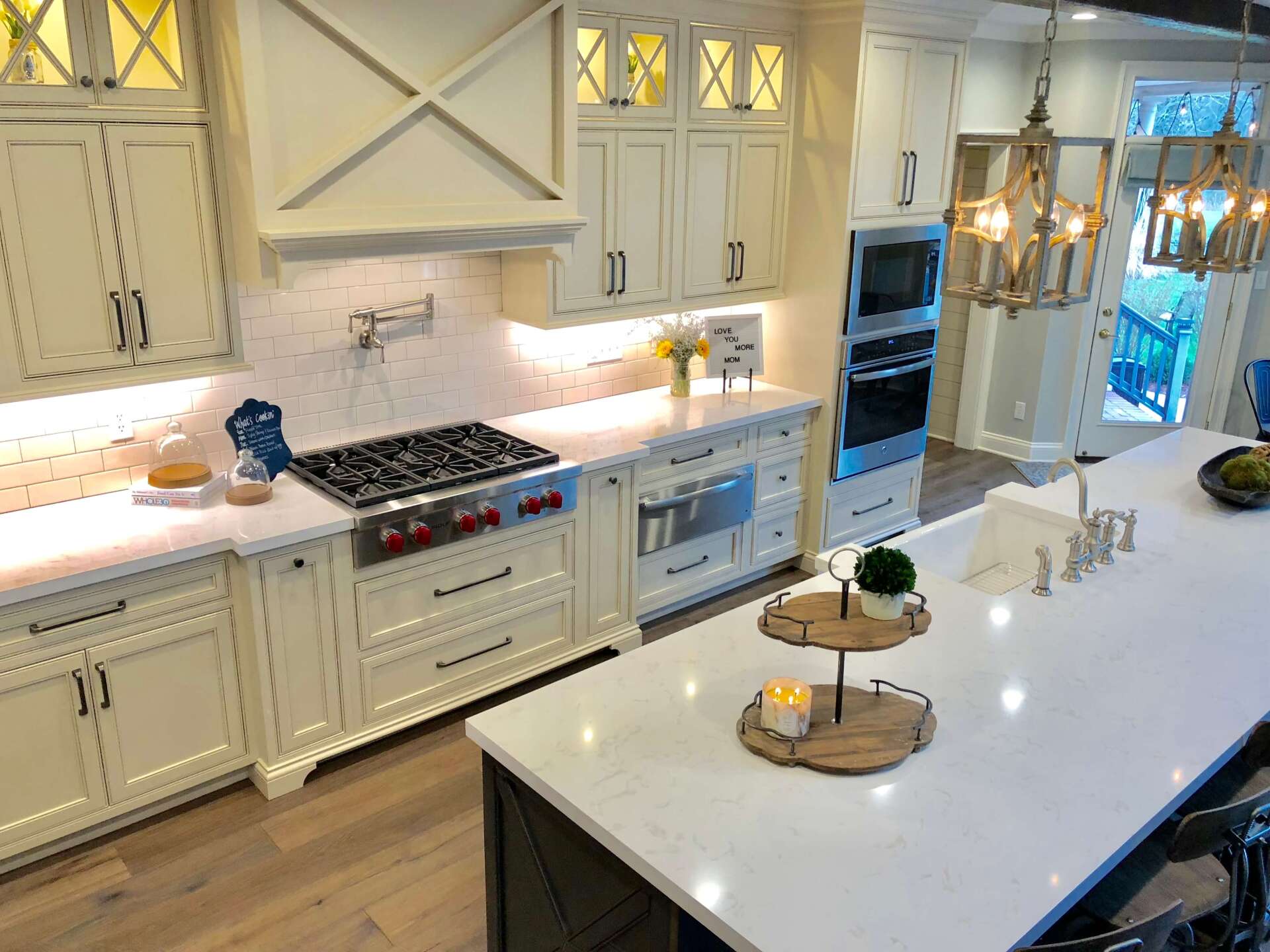 Bright white kitchen with island, built-in ovens, gas range, and glass cabinets beneath warm pendant lights