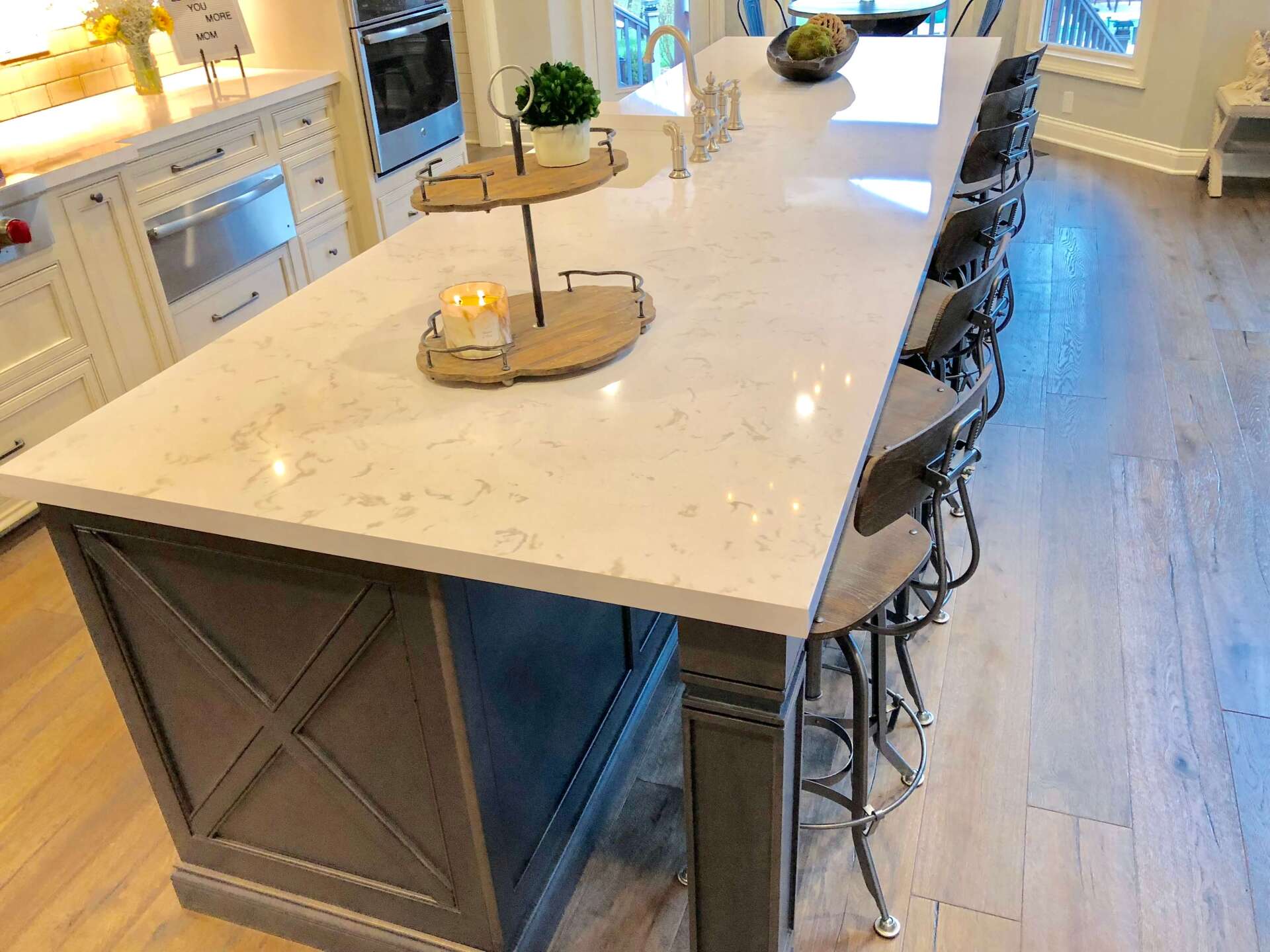Bright kitchen with a large marble island, bar stools, and warm decor by a window.