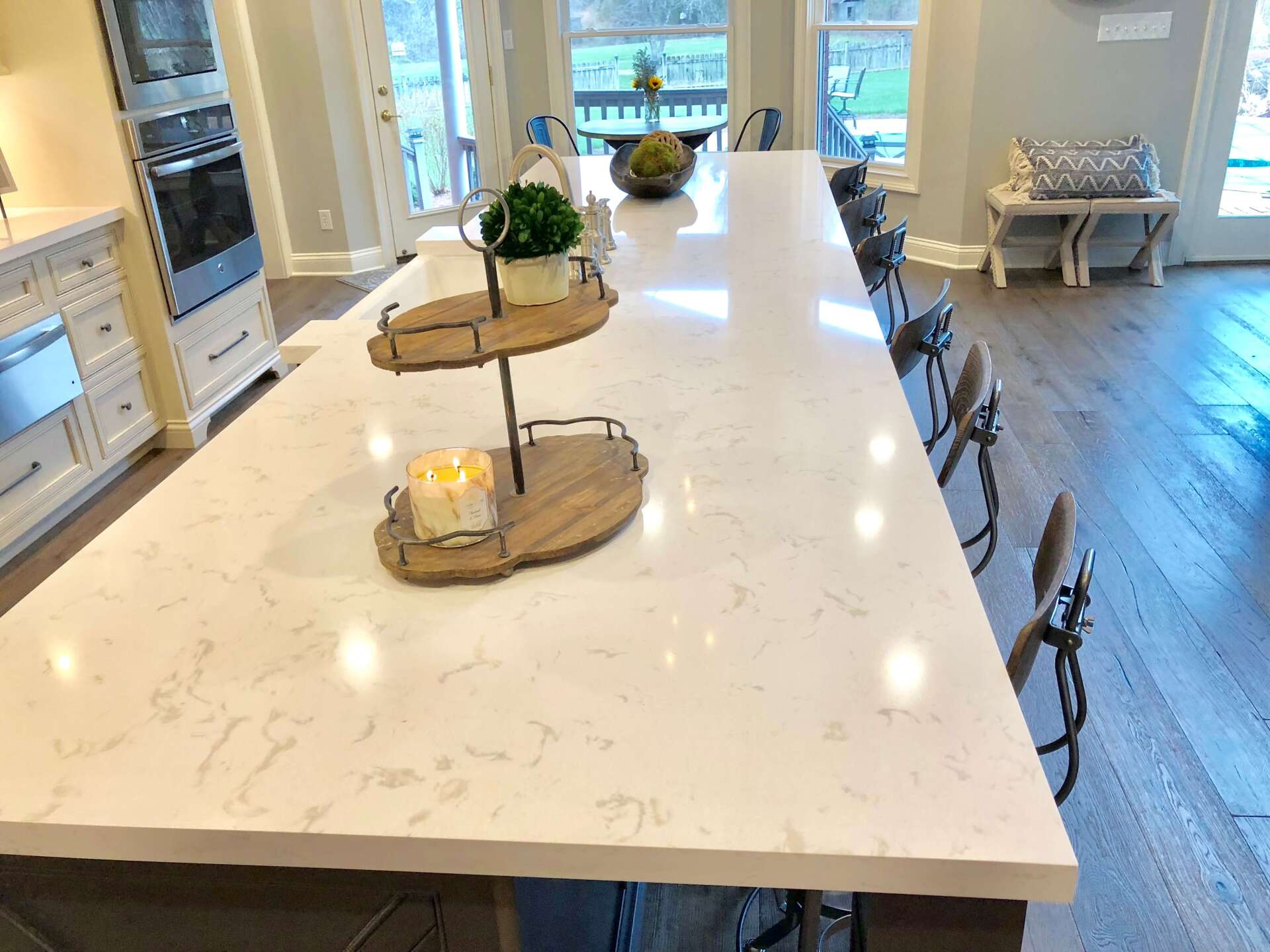 Bright kitchen with a large white island, decorative trays, and bar stools by a windowed dining area