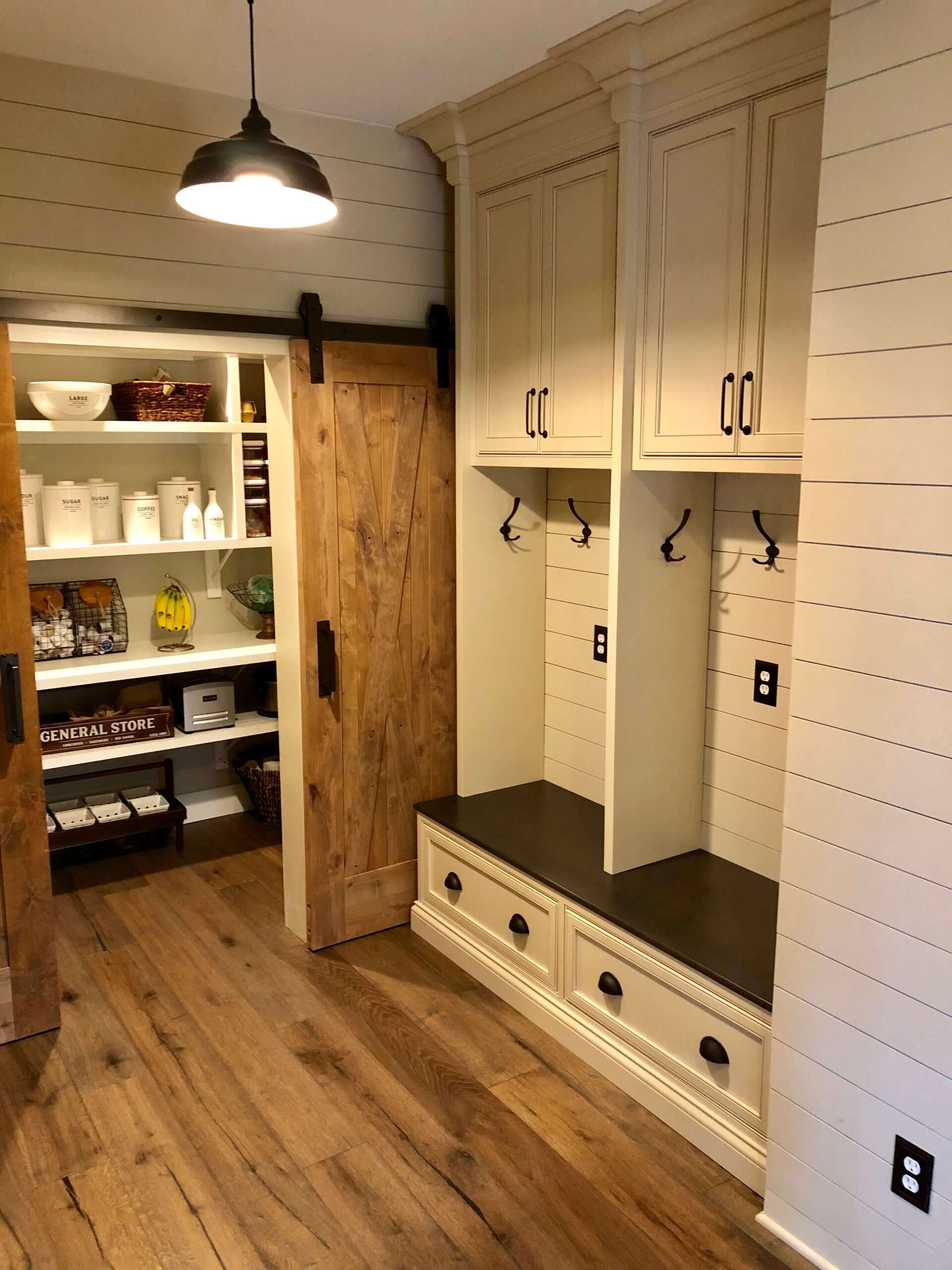 Mudroom with built-in cabinets, bench, hooks, and open pantry shelves on wood floor.
