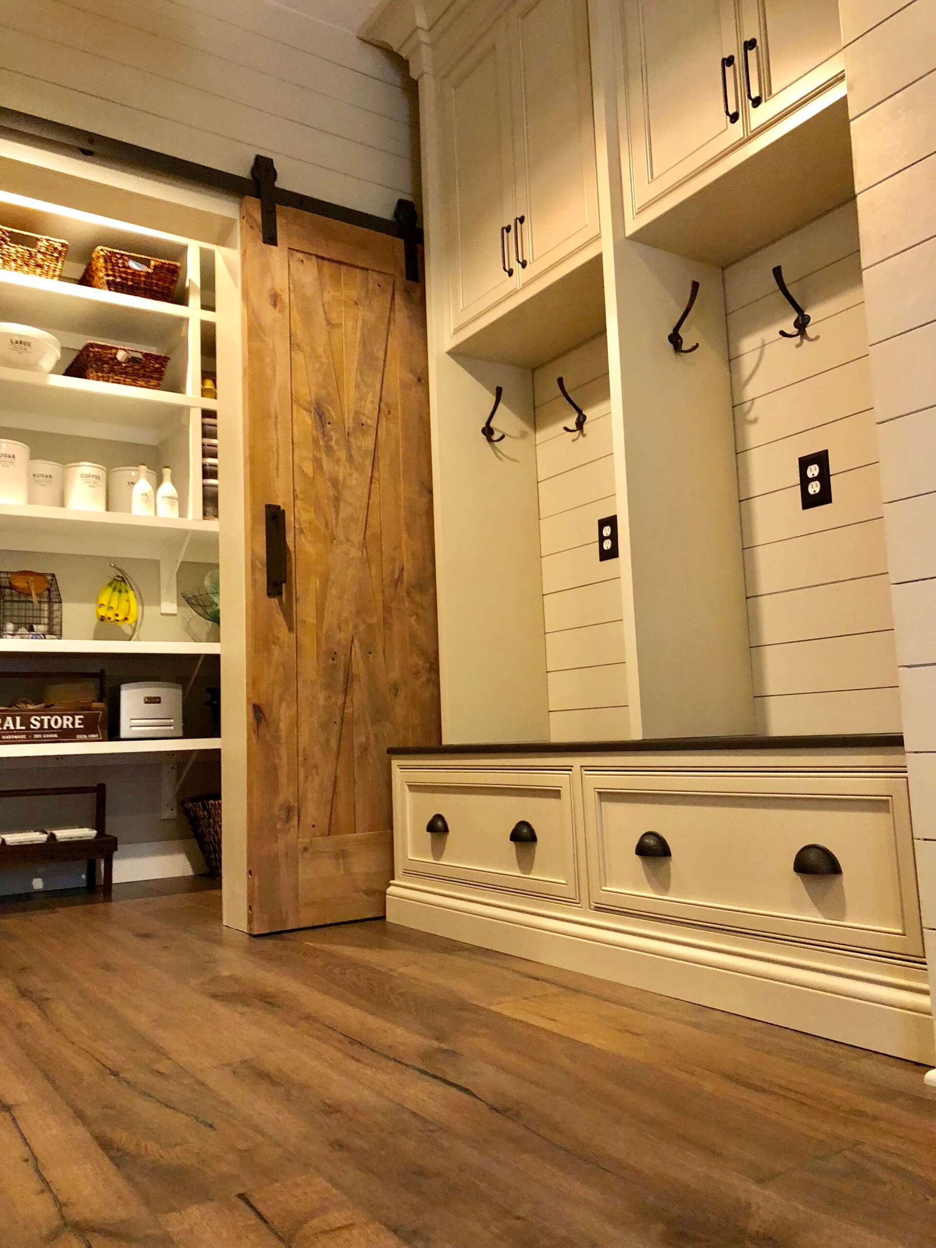 Cozy mudroom with white built-in cubbies, wood bench, open shelves, and a rustic barn-style door on wood floors