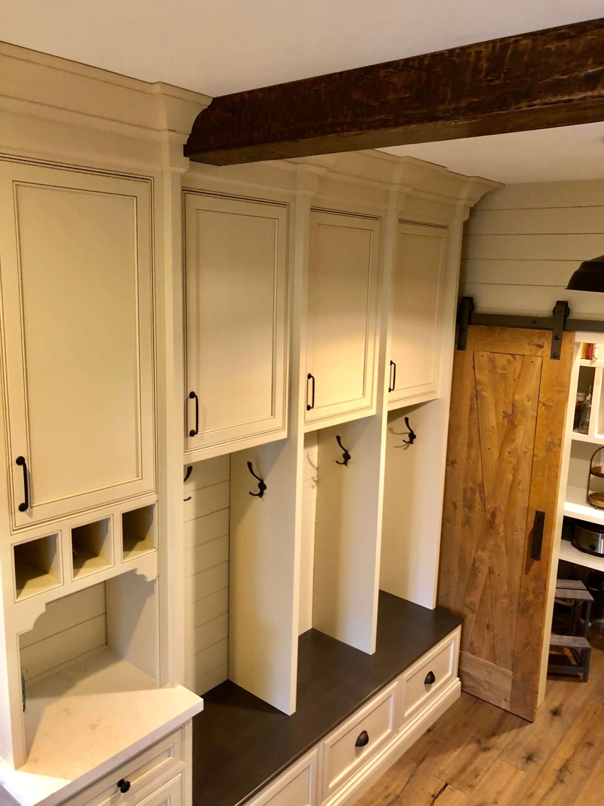 Built-in cream mudroom benches and cabinets with dark wood beams and a barn door, empty interior.