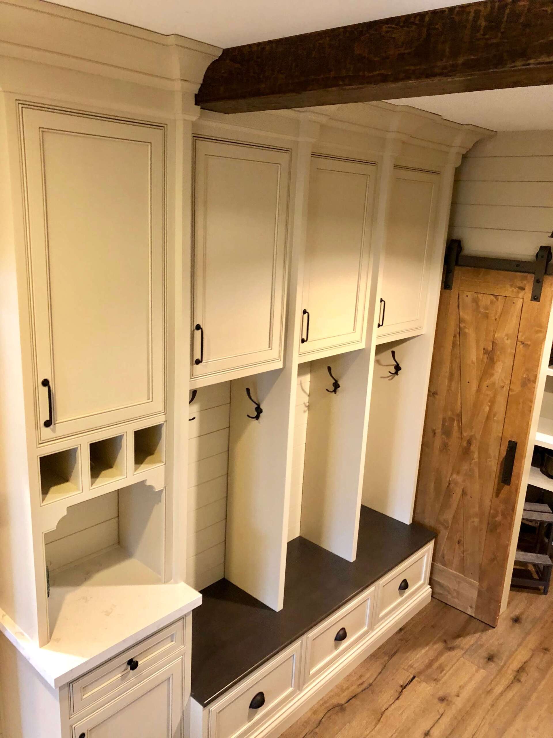 Built-in white wooden lockers with benches and black seat cushions in a mudroom or entryway