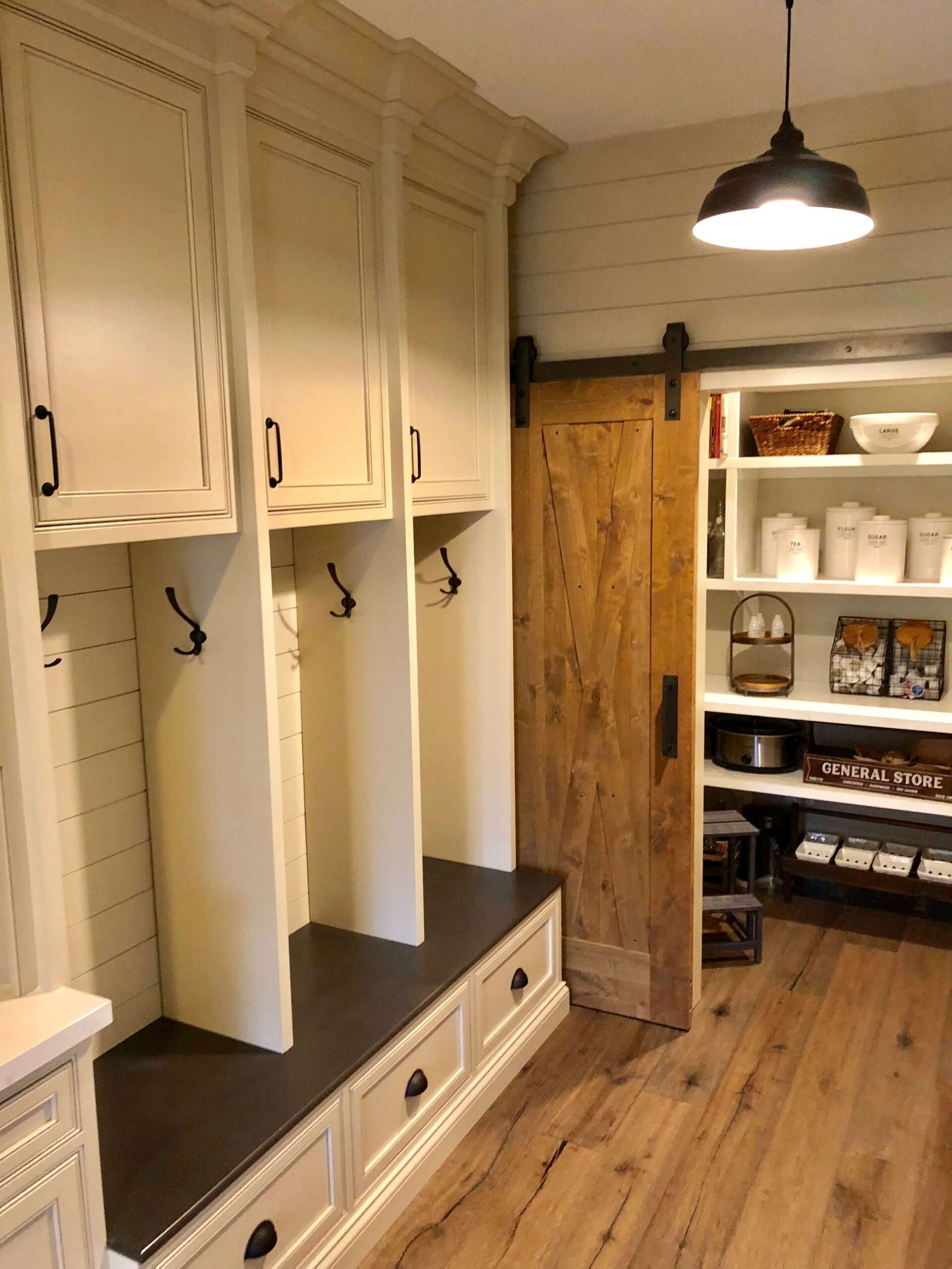 Mudroom with white built-in cubbies, dark bench, wooden sliding door, and open shelving on wood floor