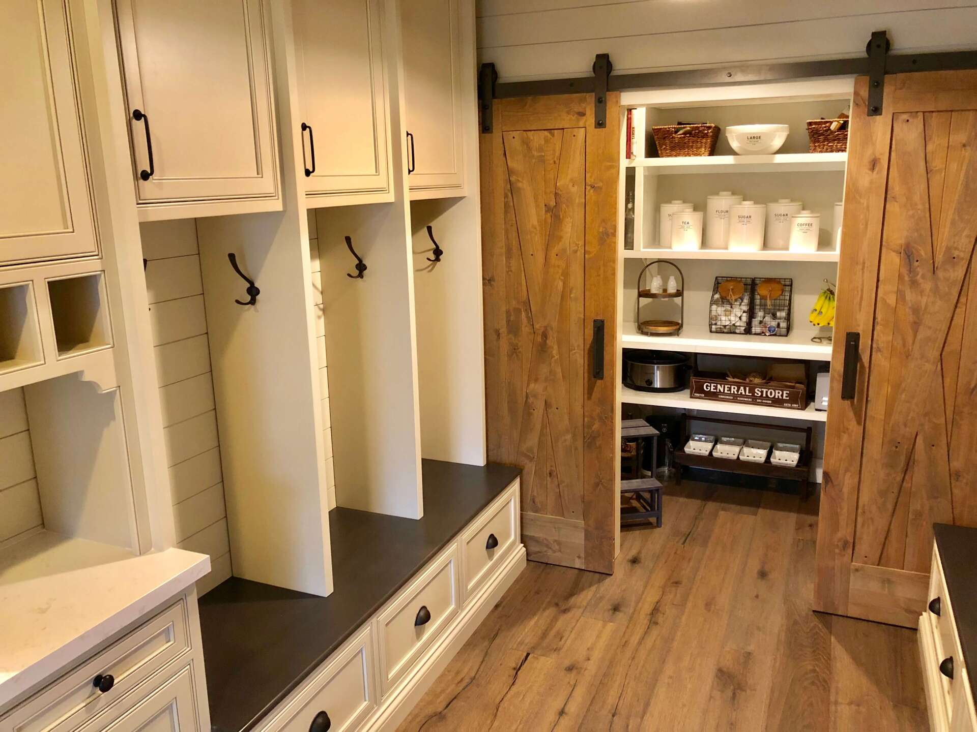 Mudroom with white cubbies and benches on left, open pantry shelves and wood floors on right