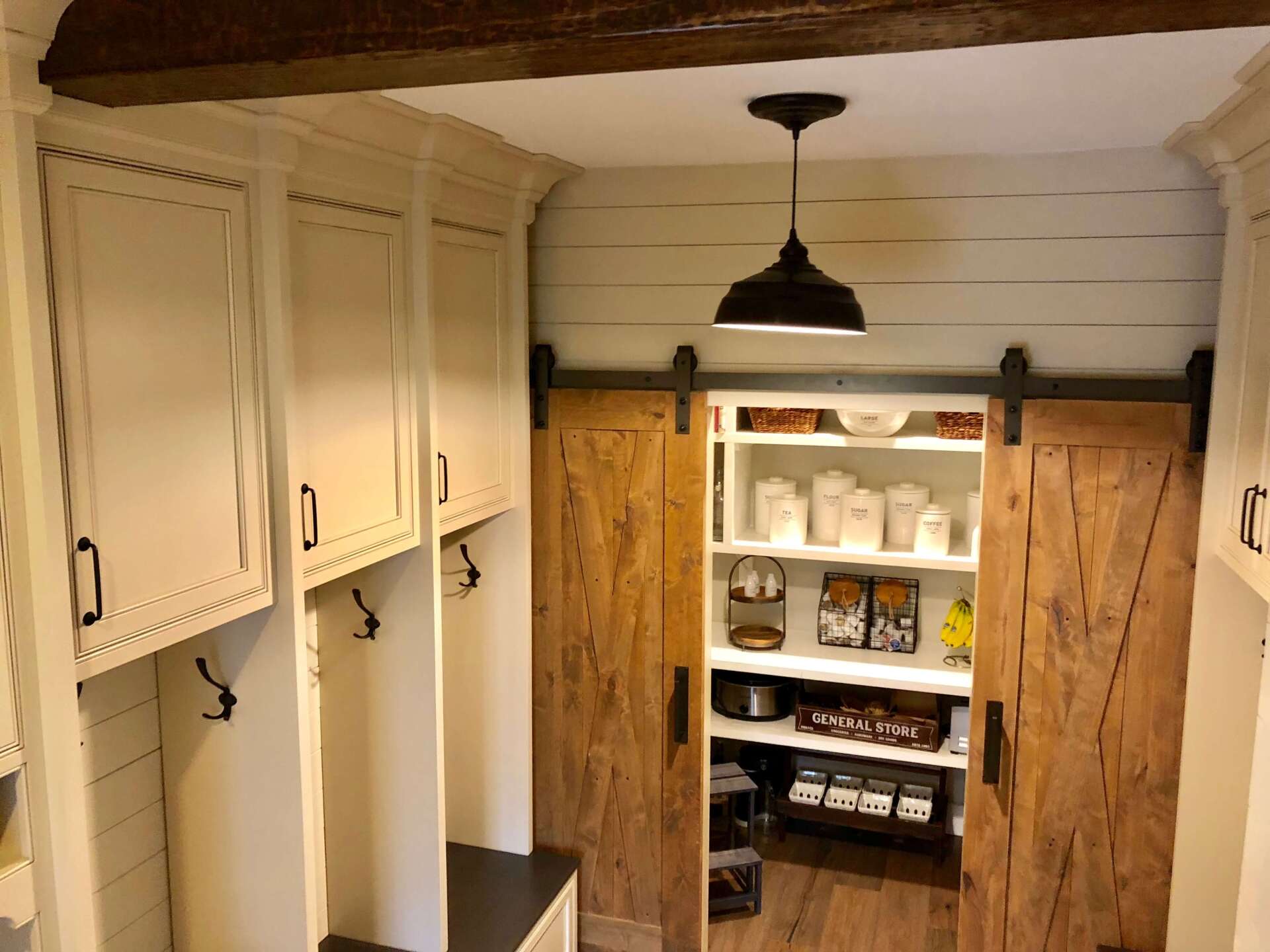 Rustic pantry with open wooden sliding doors, white shelves, and a hanging light in a narrow hallway