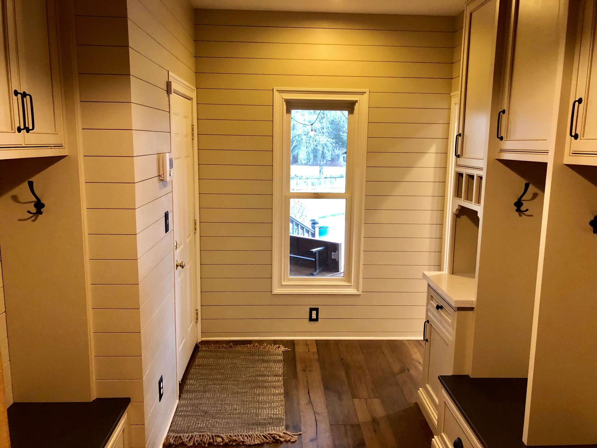 Narrow walk-in closet with beige shelves, wood flooring, and a small window at the far end.