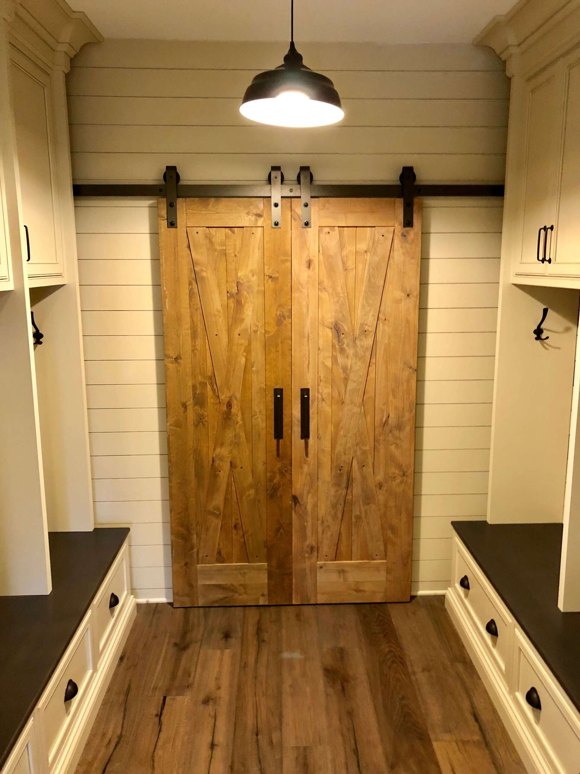 Rustic walk-in closet with wood floors, built-in shelves, and double barn doors under a hanging light.
