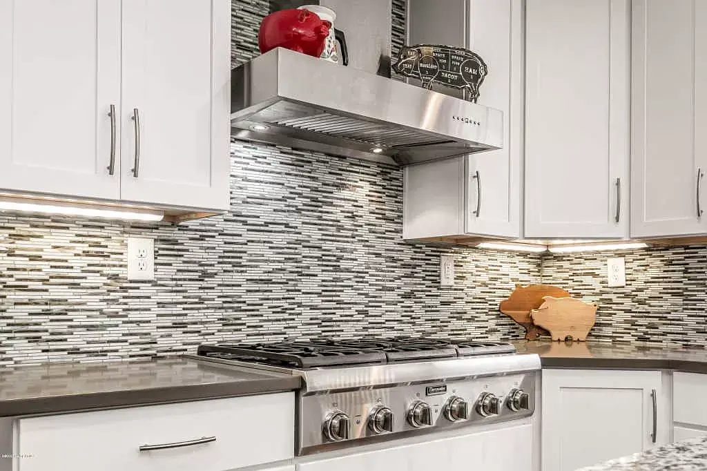 Modern kitchen with stainless steel stove, silver mosaic backsplash, and white cabinets