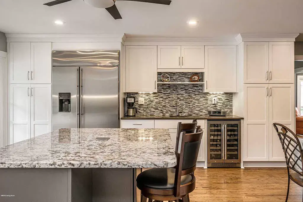 Modern kitchen with stainless steel fridge, white cabinets, granite island, and hardwood floor