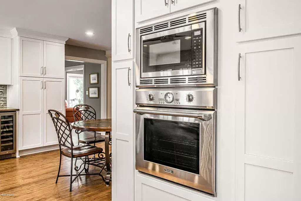 Bright white kitchen with built-in stainless steel oven and a small dining table on hardwood floor