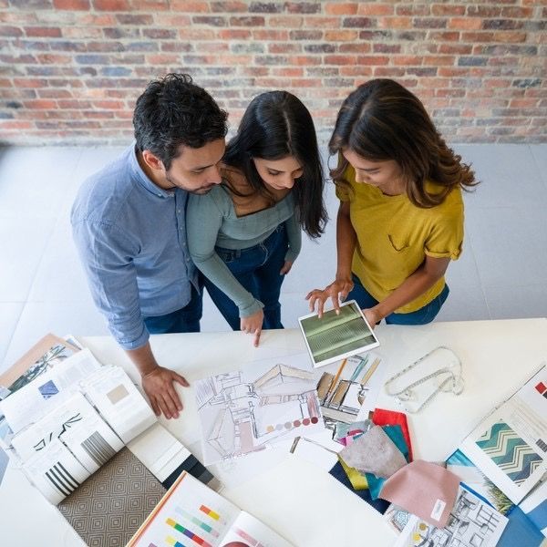 Three people reviewing design sketches spread across a table in a studio-like workspace