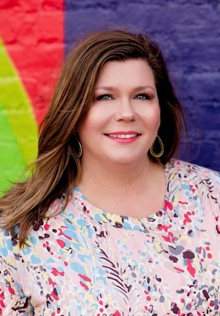 Woman smiling in a pastel floral blouse against a colorful red, green, and purple wall