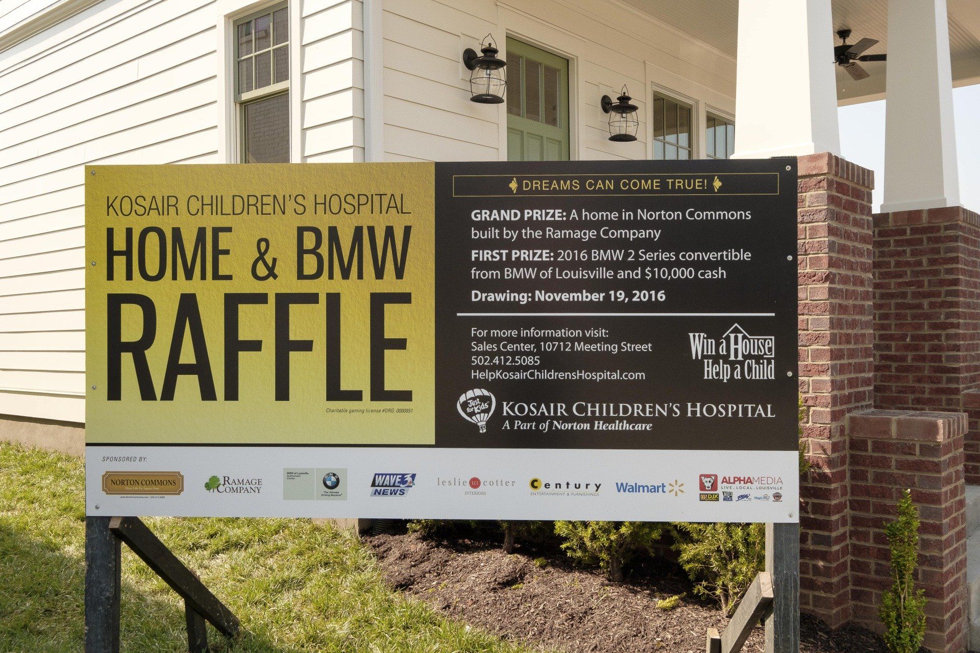 Outdoor sign advertising a “Home & BMW Raffle” for a hospice charity, with sponsor logos on a white base panel
