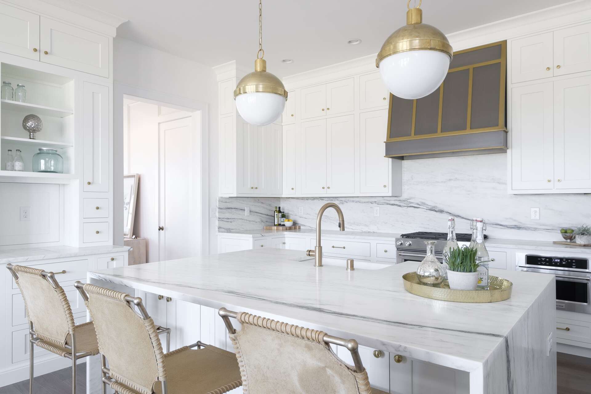 Bright white kitchen with marble island, gold pendant lights, and beige upholstered stools