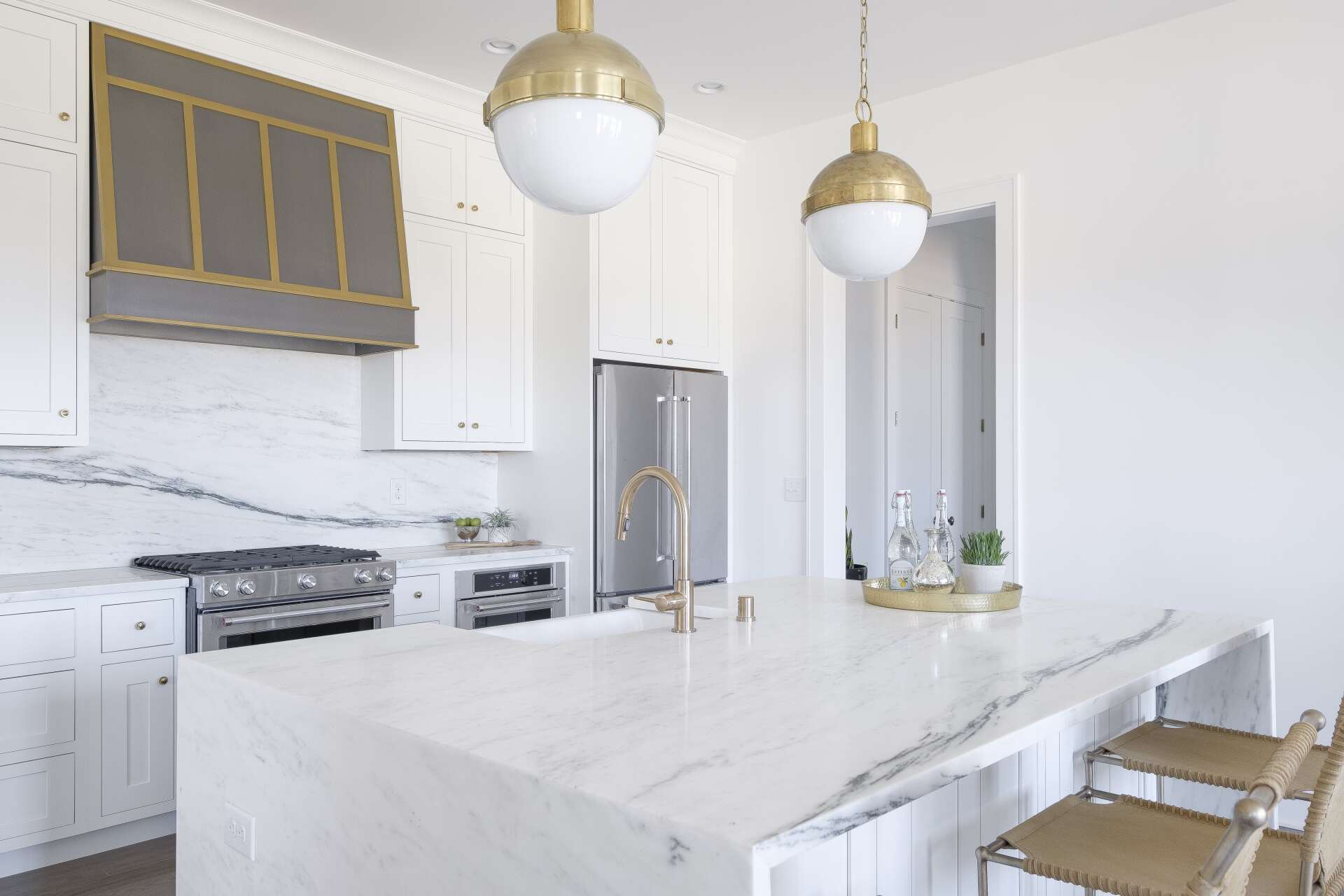 Bright white modern kitchen with marble island, stainless appliances, and brass pendant lights