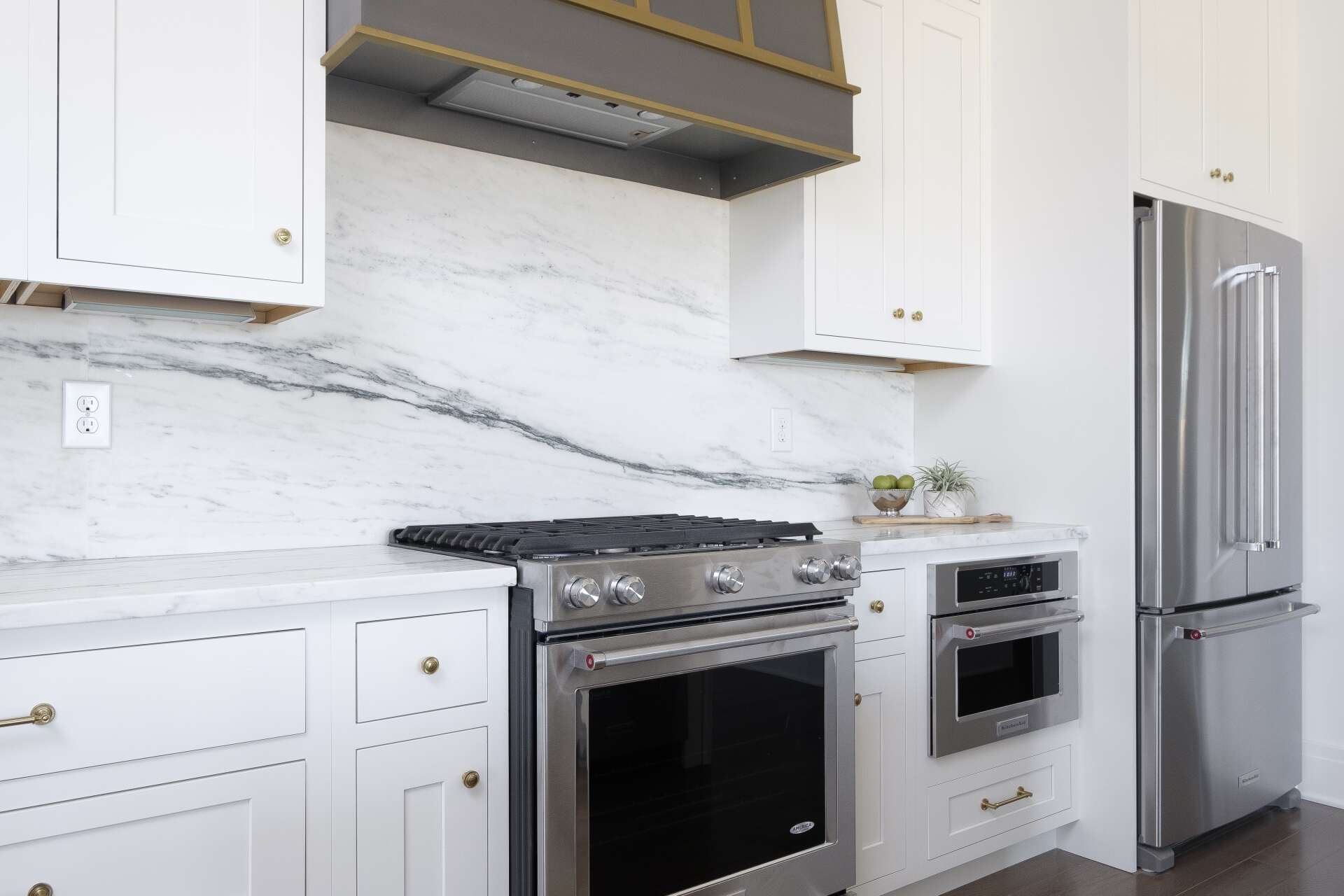 Modern white kitchen with marble backsplash, stainless steel stove, oven, and refrigerator