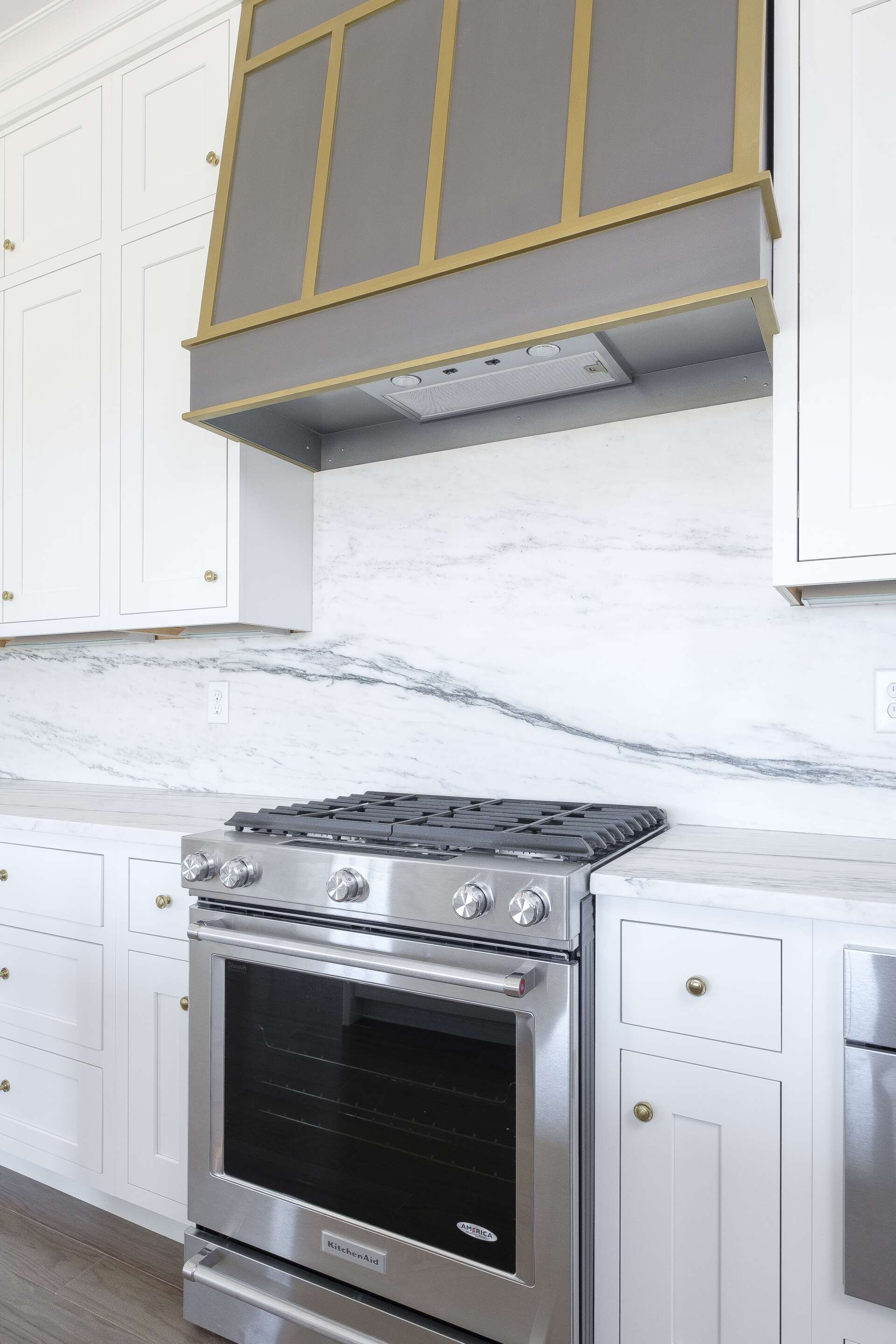 Modern kitchen with stainless steel range, white cabinets, and marble-pattern backsplash