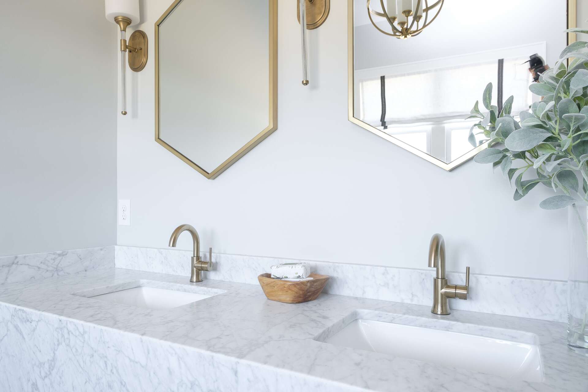 Bright white bathroom vanity with marble countertop, gold fixtures, mirrors, and a small wicker basket.