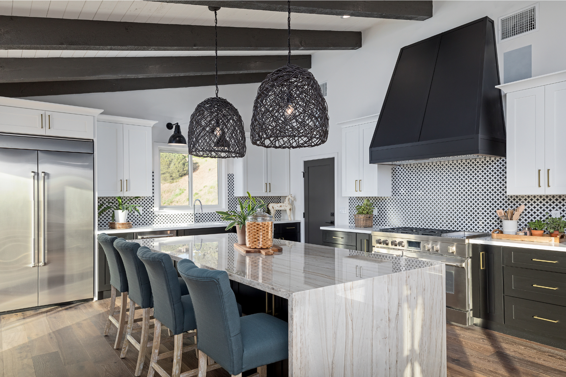 Modern kitchen with white island, blue barstools, pendant lights, stainless fridge, and black range hood