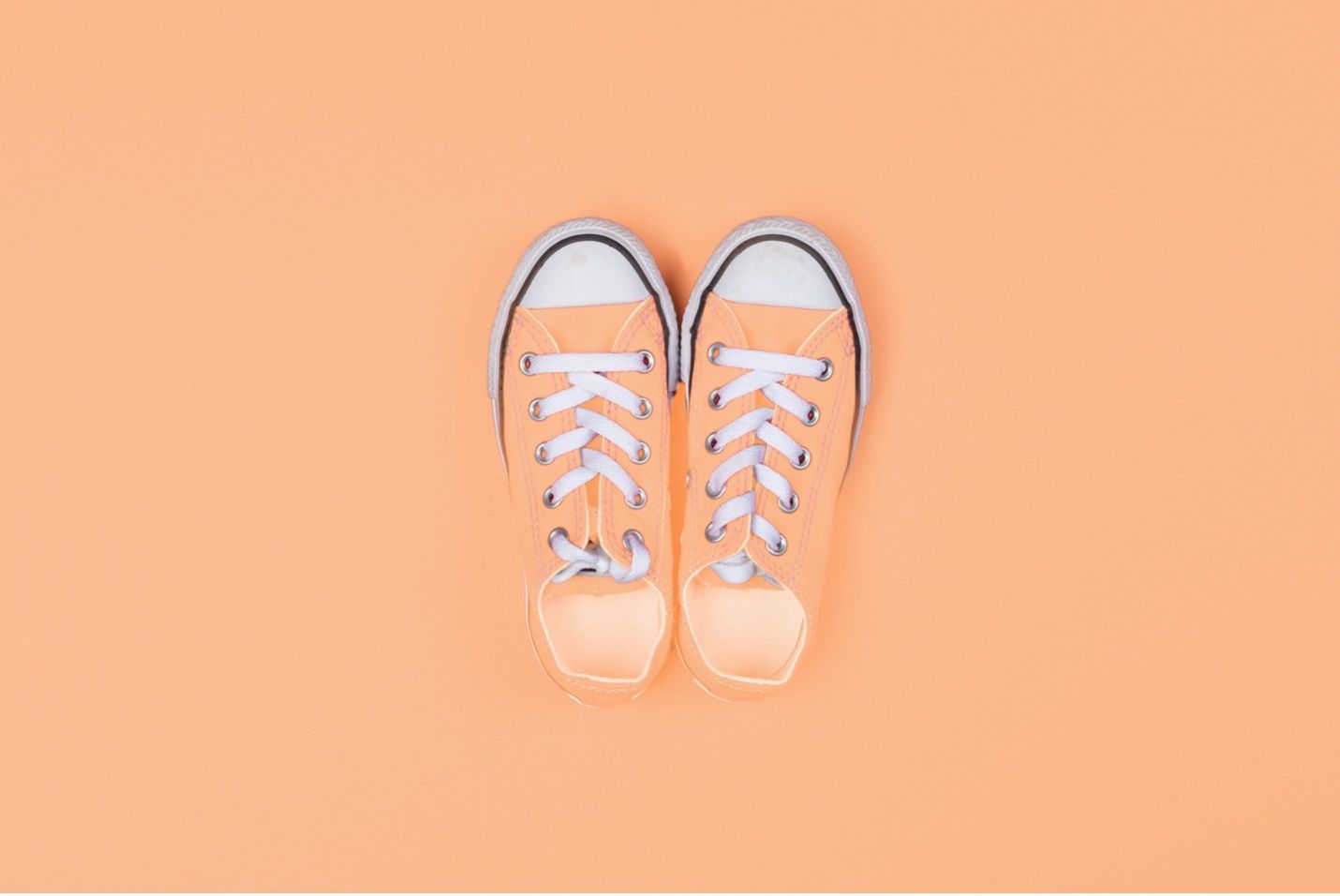 A pair of white sneakers on a peach background.