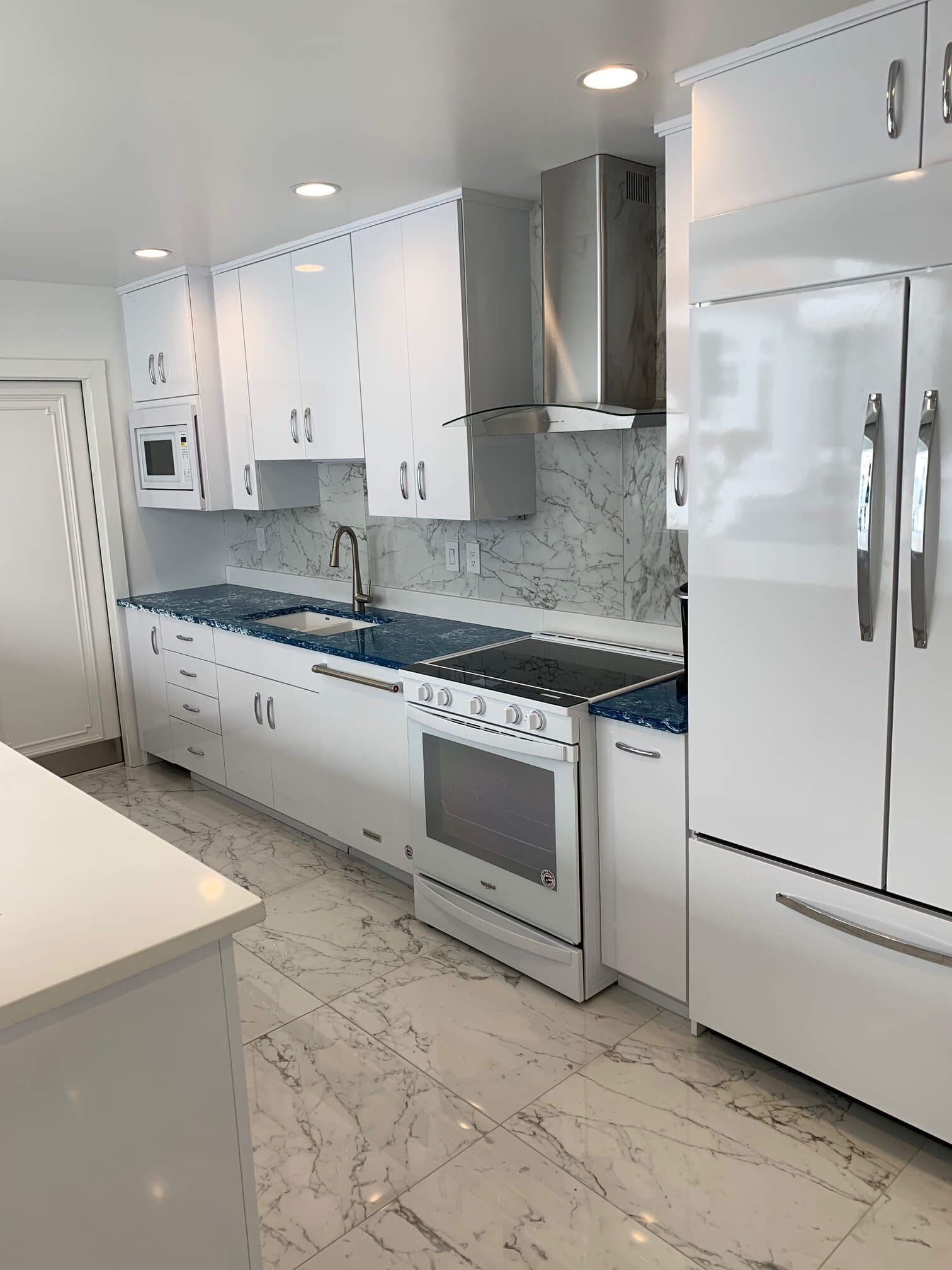 Modern white kitchen with marble floor, white cabinets, blue backsplash, and stainless steel appliances
