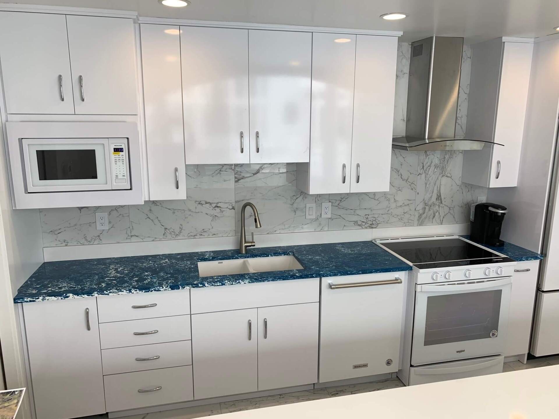 Modern white kitchen with blue countertops, white cabinets, stainless range hood, and built-in microwave