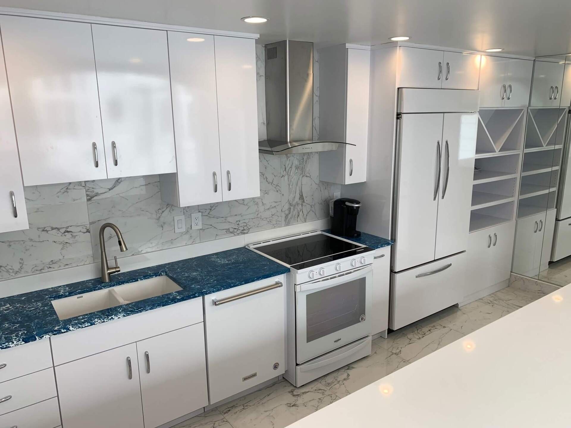 Modern white kitchen with blue countertops, stainless steel appliances, and tile backsplash