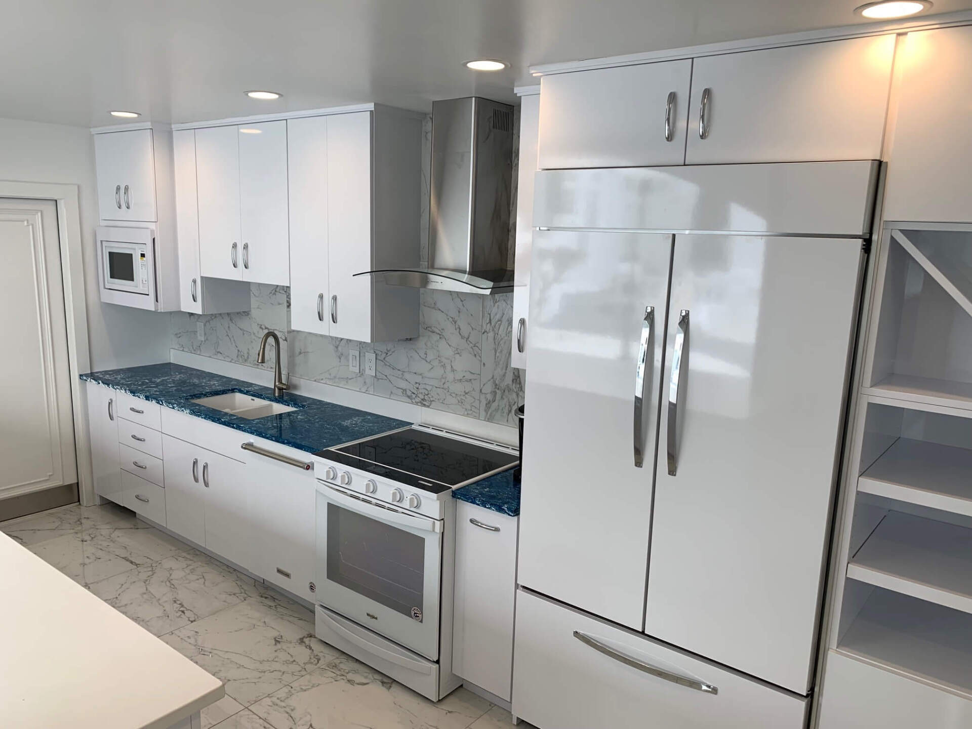 Modern white kitchen with stainless appliances, blue countertops, and a white refrigerator