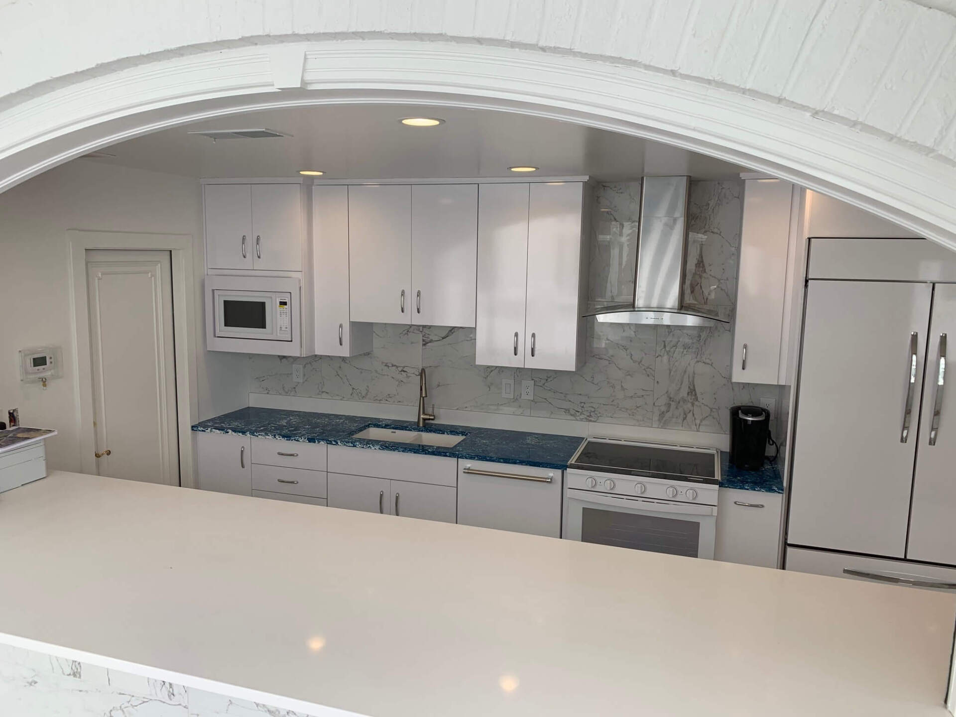 Bright white kitchen with arched opening, marble counters, stainless appliances, and blue backsplash accents
