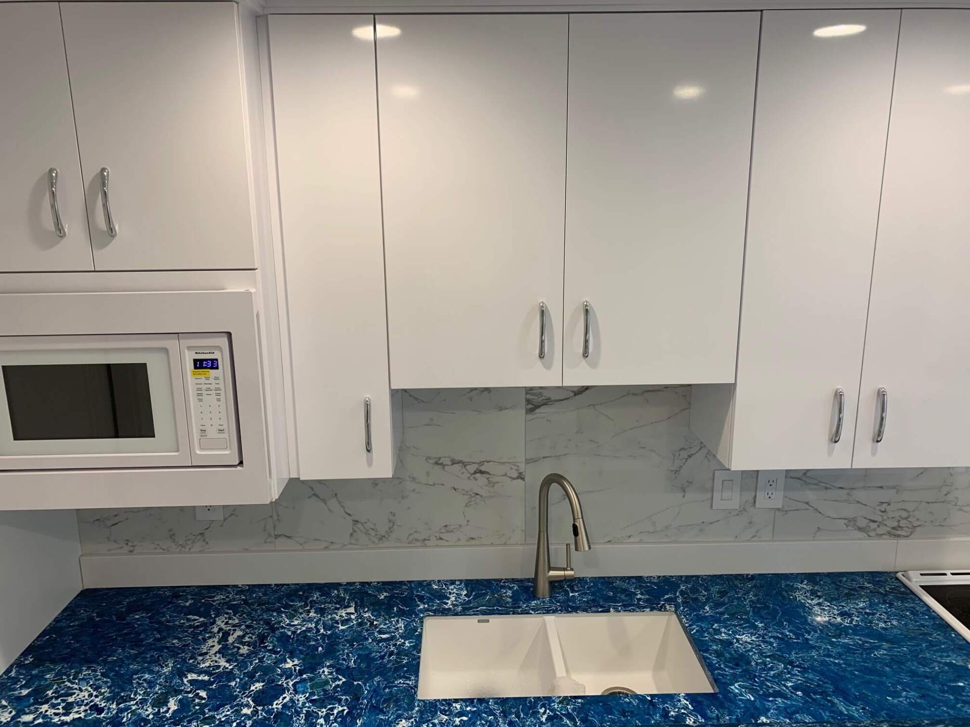 White kitchen with blue countertops, white cabinets, microwave, and sink with faucet.