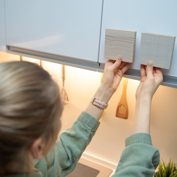 Person placing two sample tiles on a kitchen cabinet, with under-cabinet lights on