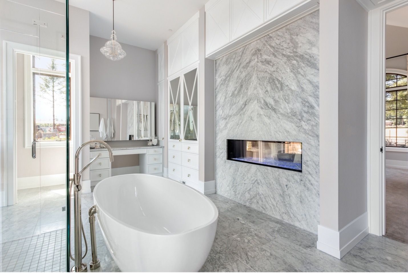 Modern bathroom with a freestanding tub, marble fireplace wall, and glass shower enclosure