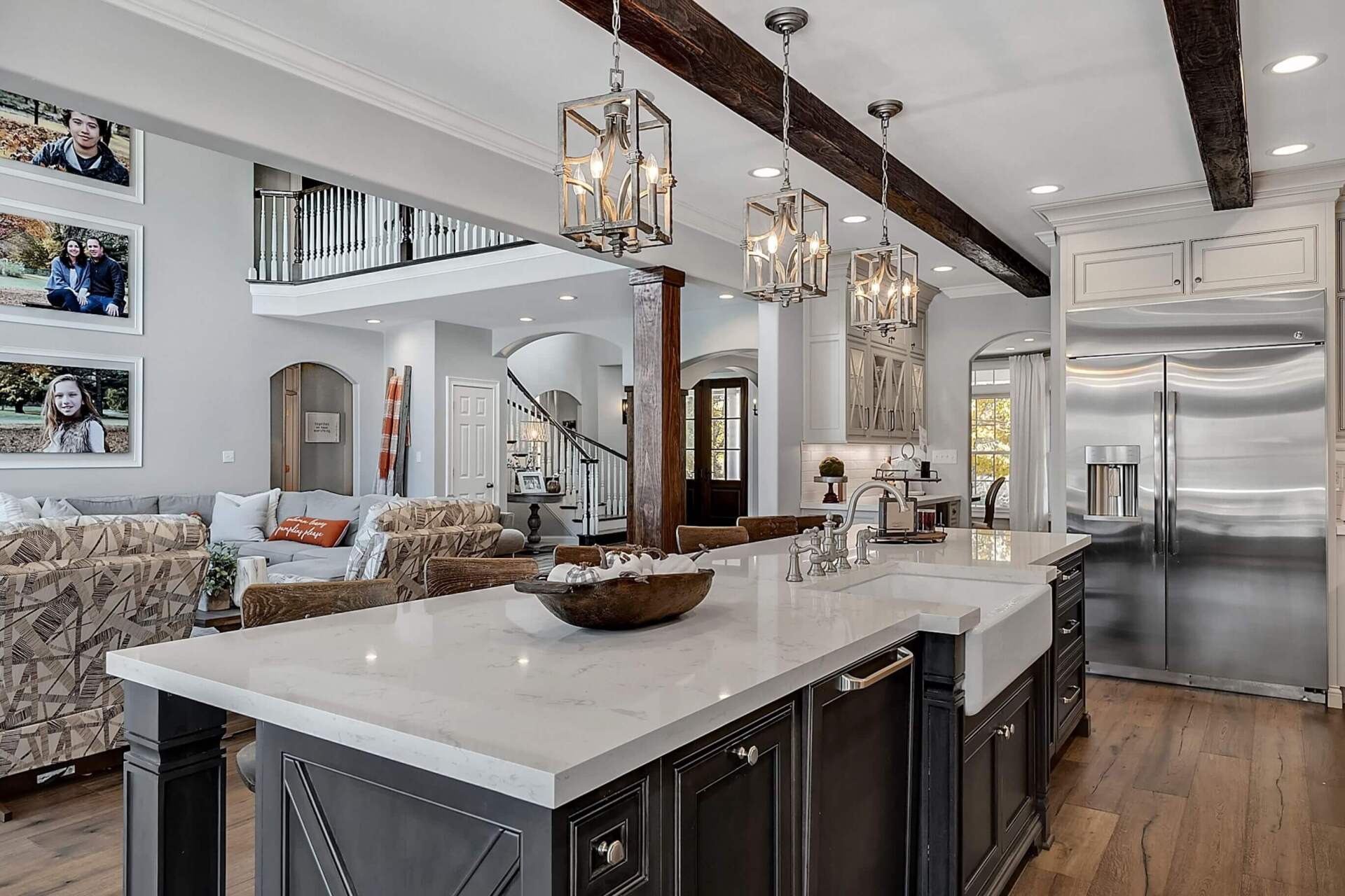 Bright modern kitchen with white island, dark cabinets, stainless fridge, and pendant lights