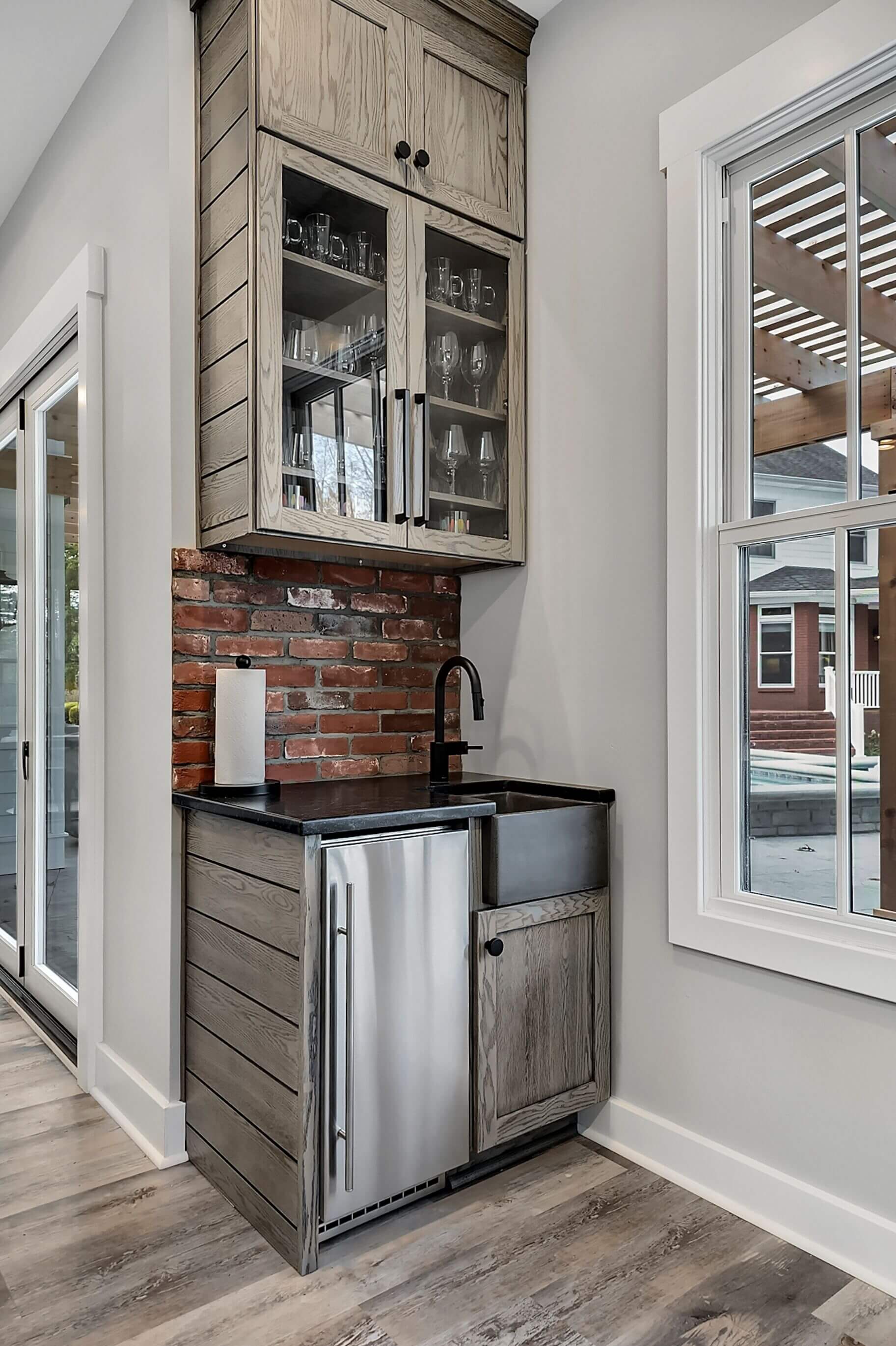Compact kitchen nook with gray cabinets, brick backsplash, and a small stainless mini fridge by a window