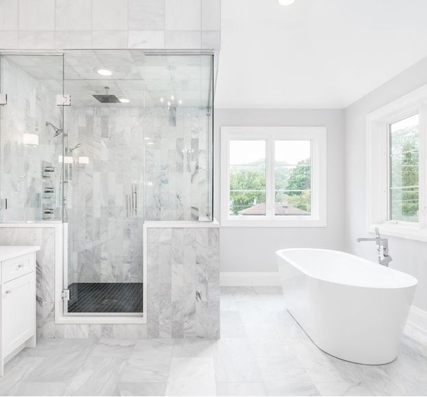 Bright white bathroom with glass shower and freestanding tub by windows