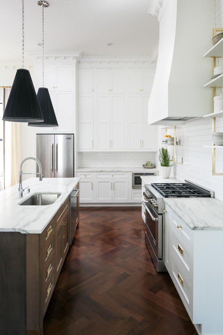 Bright modern kitchen with white cabinets, marble counters, stainless fridge, and dark wood herringbone floor